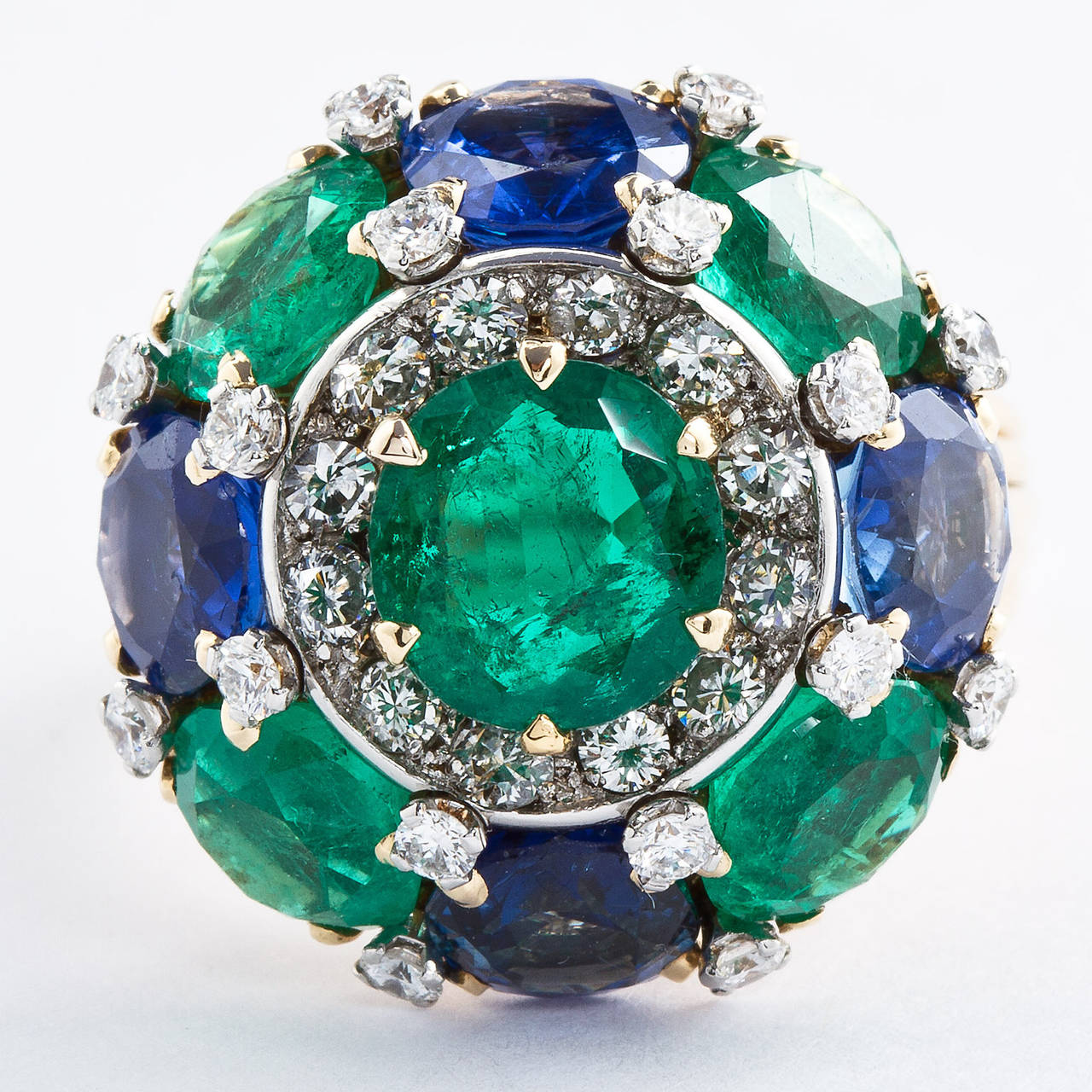An emerald and sapphire dome ring with diamond accents set in 18k yellow gold. Contains approximately 5.25 carats of emeralds and approx. 3.40 carats of sapphires in round brilliant cut style. A further approx. 1.00 cts total of round brilliant cut