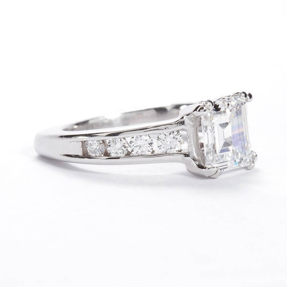 A four prong platinum ring set with a 1.74 carat D color SI1 clarity rectangular step cut diamond with four round-brilliant channel set diamonds on either side.  A small diamond is bezel set on either side of the gallery profile for an additional