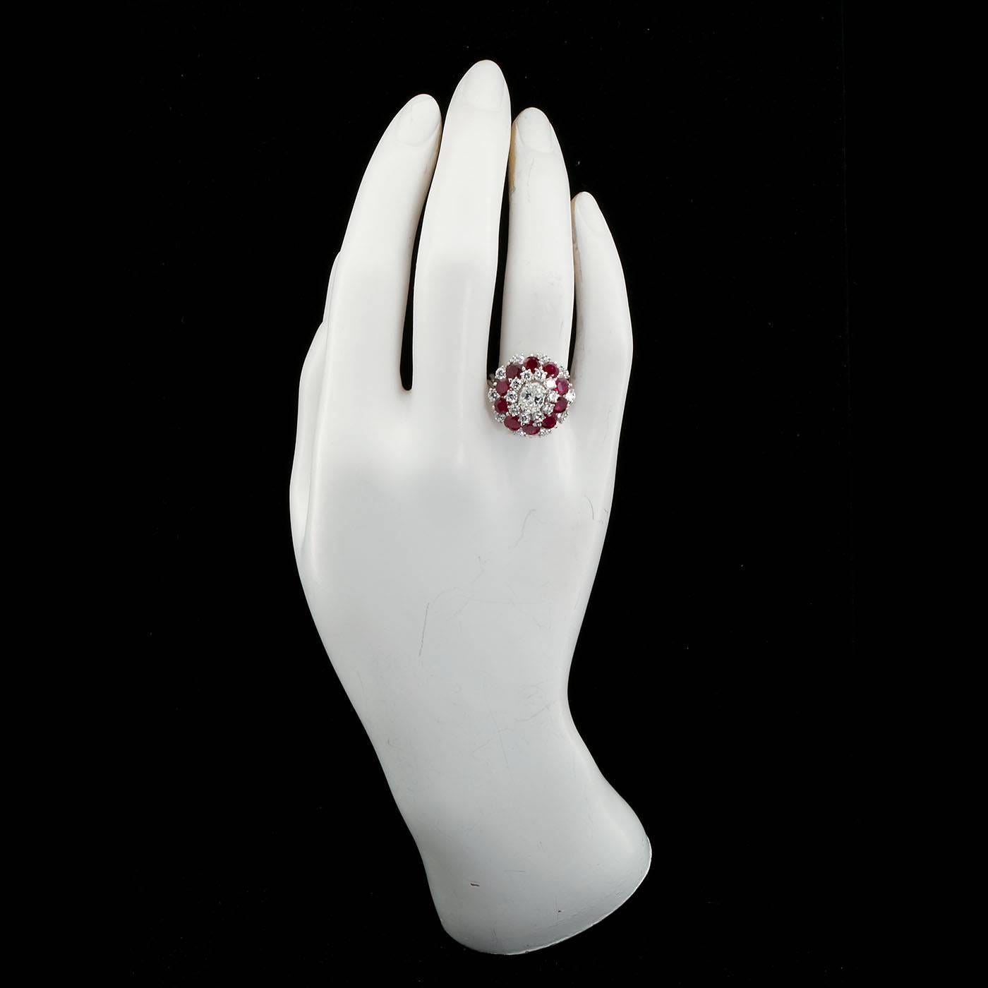 A diamond and ruby cluster ring set in platinum comprised of one approx. 0.90 ct. oval brilliant cut diamond of high color and VVS clarity surrounded by ten [10] round brilliant cut deep reddish rubies weighing approx. 2.50 cts.and another two rows