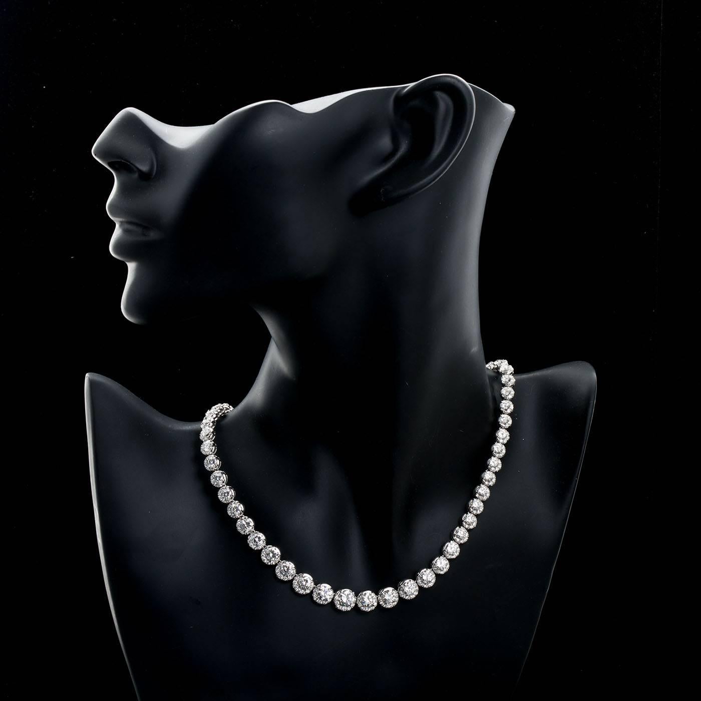 A unique diamond in platinum Rivieré necklace set with approximately twenty carats of very high quality (G+ color VS clarity) fine round brilliant cut diamonds set in four-prong mountings with a drape of diamond pave beneath each diamond.  Largest
