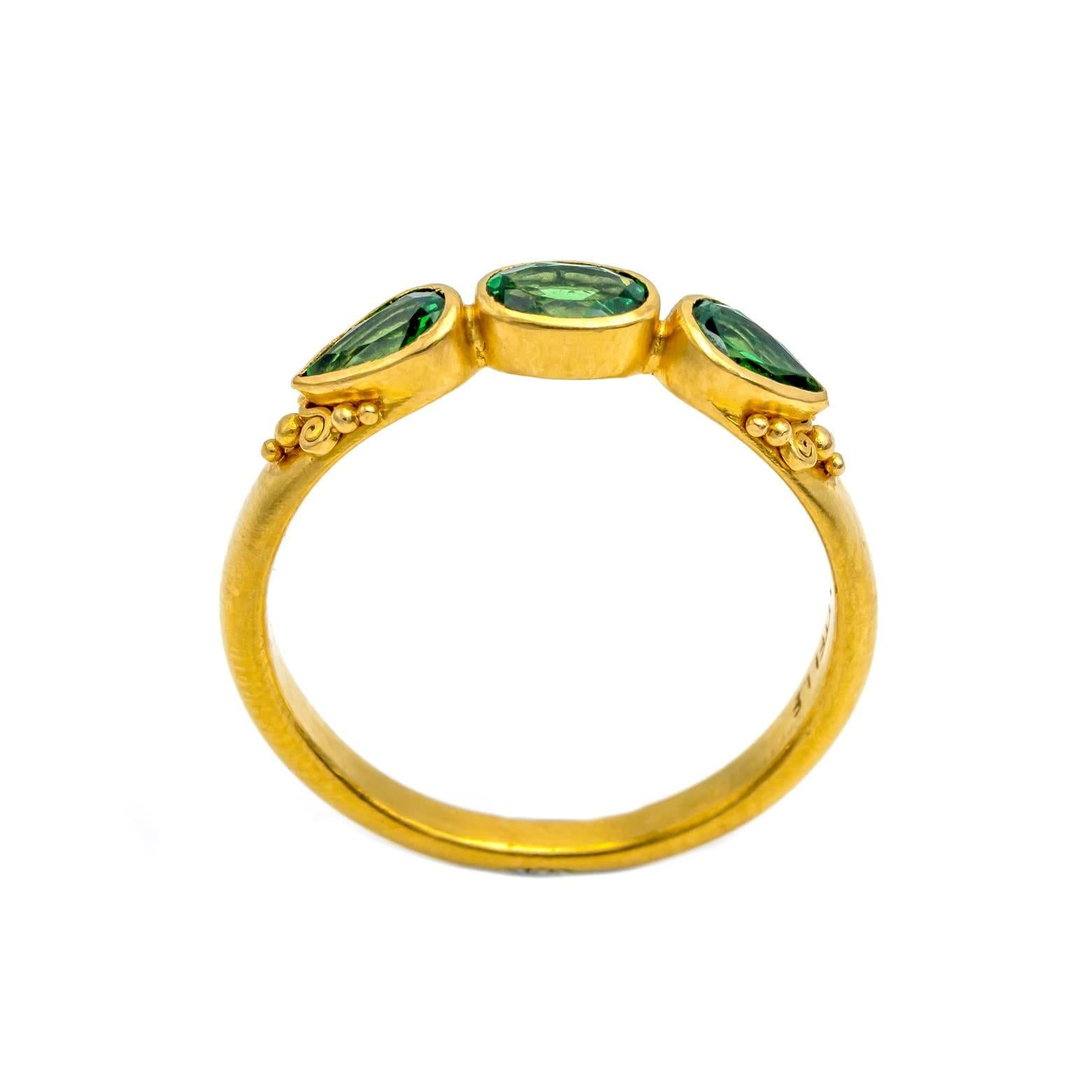 Three glowing green tsavorite garnets are set next to each other in 18K yellow gold. Bezel set with two pear shapes pointing outward and a central oval, this ring mesmerizes! The high carat satin finish is regal with tiny granulation and mini
