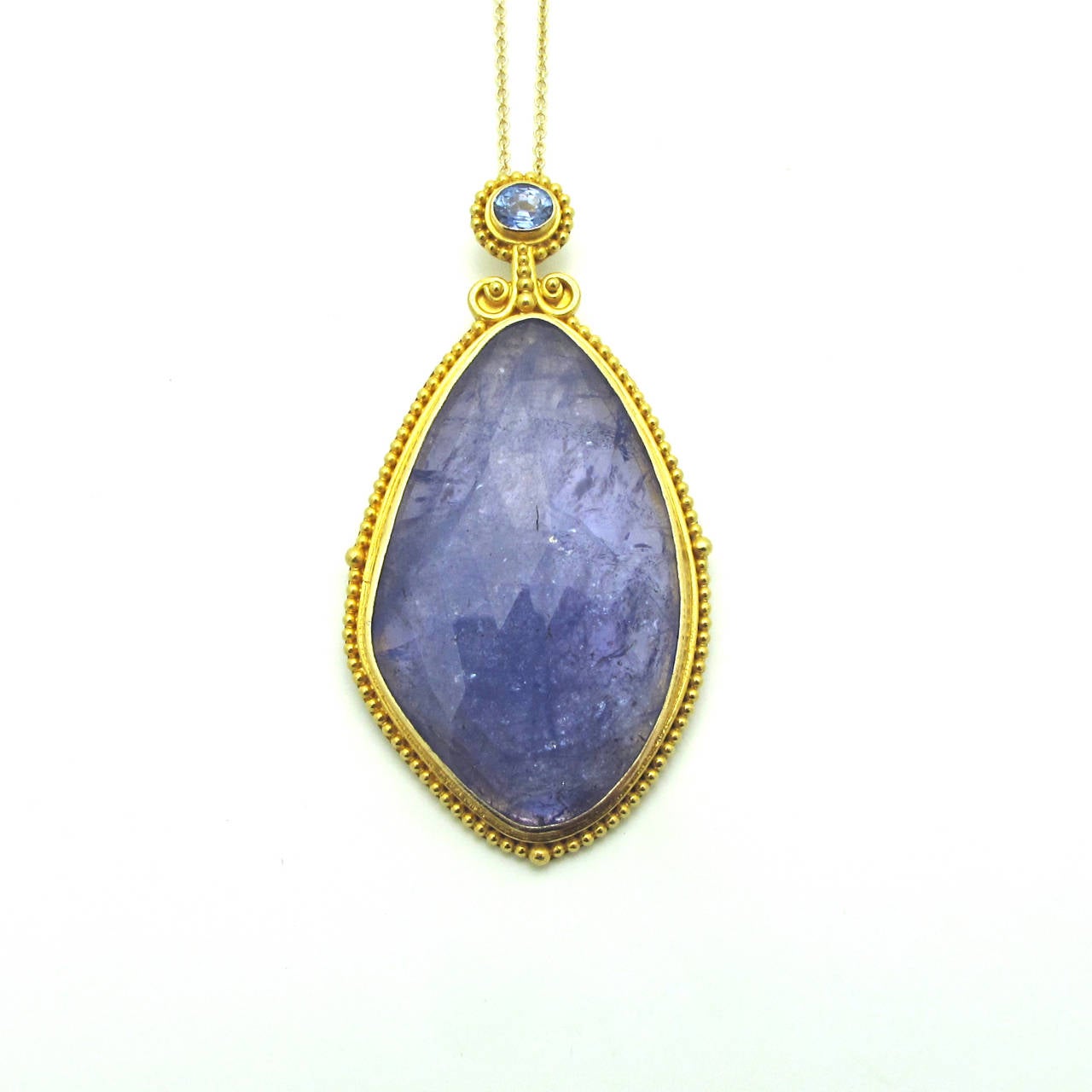 This raw faceted Tanzanite stone is elegantly encased in 18k gold beading with a stunning sapphire at the crown. It is suspended from a fine gold chain but could easily be added to a beaded necklace or a heavier chain of your choice.The tanzanite