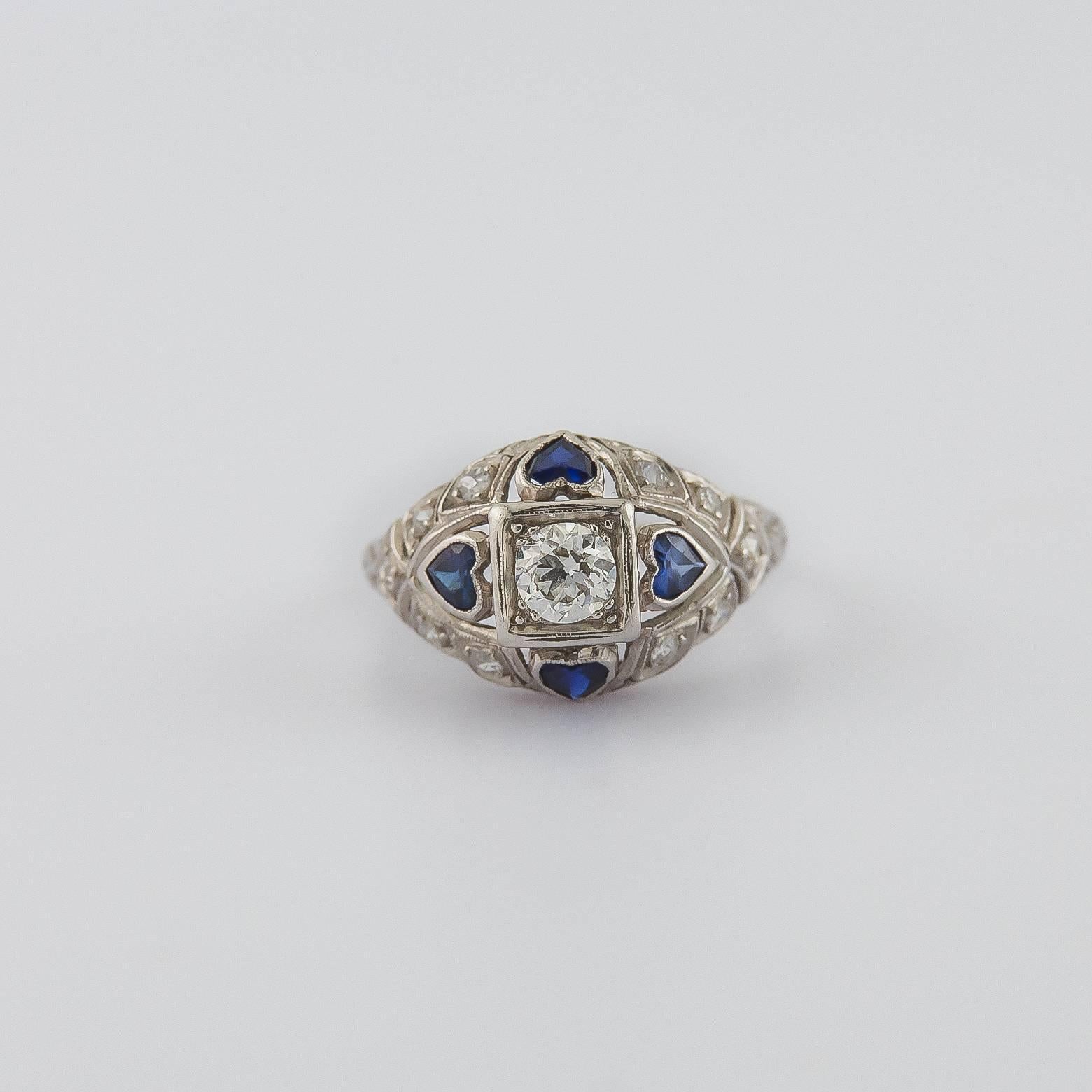 This antique and vintage style heart sapphire and diamond ring is full of beauty and romance! The central diamond is 0.25 carats and the there is a surrounding diamond pave around the deep blue sapphires set in platinum! Size 5.75