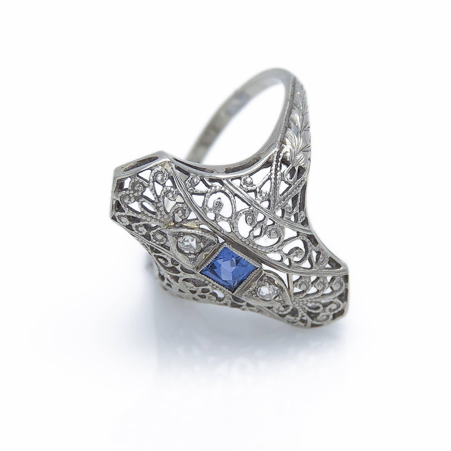 This is a unique and detail oriented piece with intricate filigree work classic of the 1930's Art Deco Era. Adorned with 2 diamonds equaling 0.05 carats and a square blue sapphire in the middle (0.13 carats) this piece exudes brilliance like a