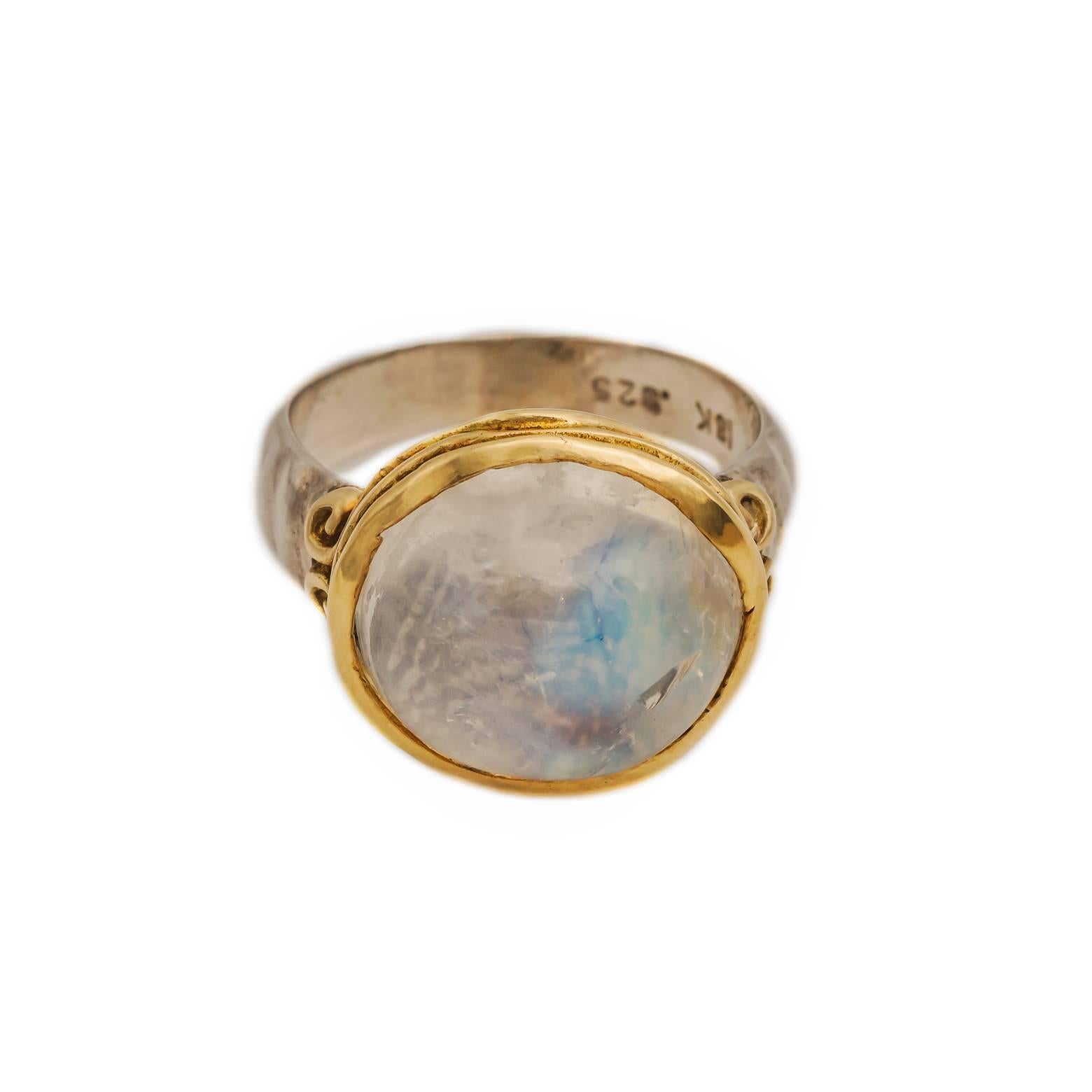 This mysterious and regal large oval 10 carat moonstone ring comes in a two-toned setting and band. The wavy 18K yellow gold bezel has two spirals on each side with a substantial satin finish band. This ring is very romantic and has an ancient