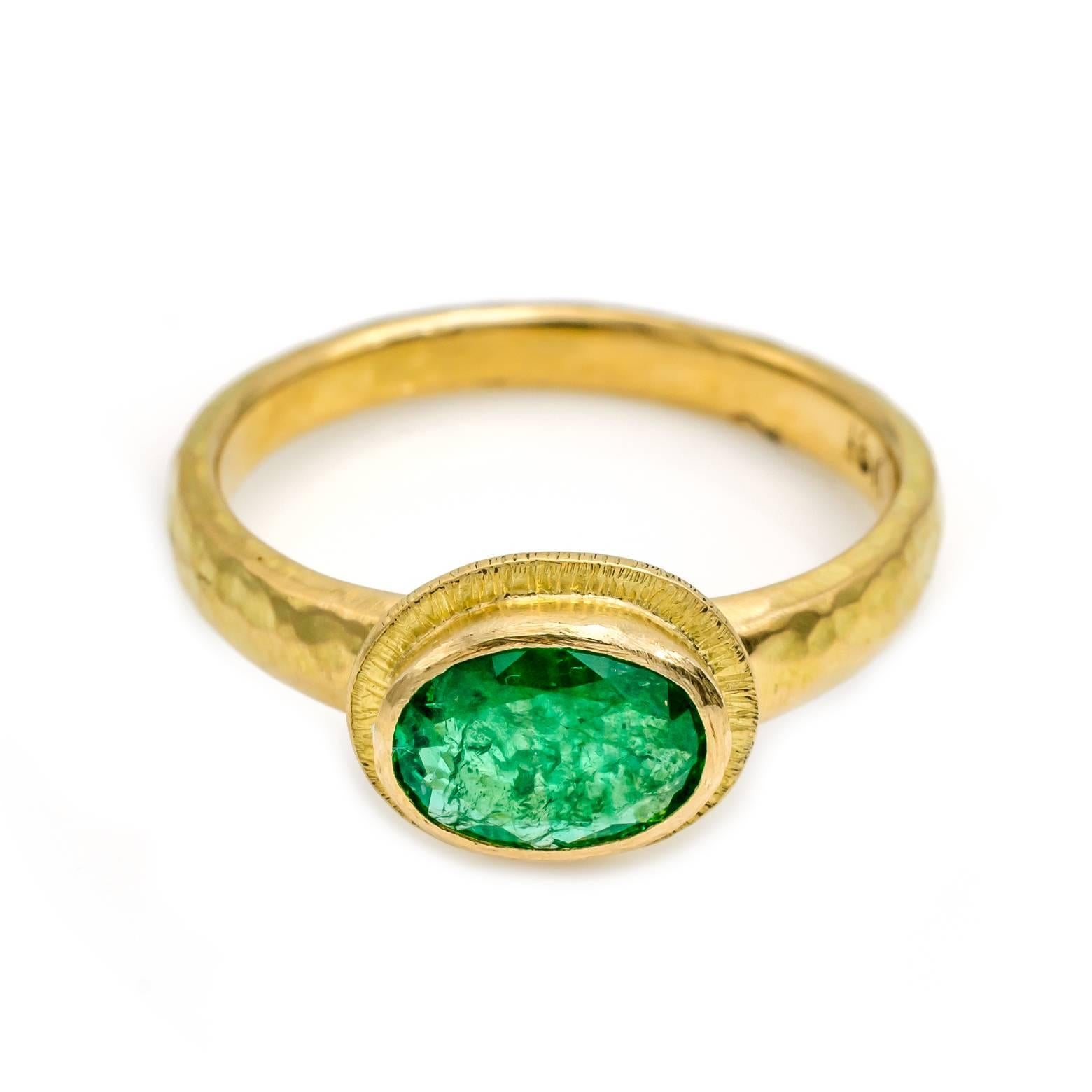 This saturated grassy green emerald ring is set in a textured bezel with lines radiating like the sun and a hammered band that is thick and substantial. Unique, artistic, and glamorous this ring is sure to be mesmerize your emerald desires and