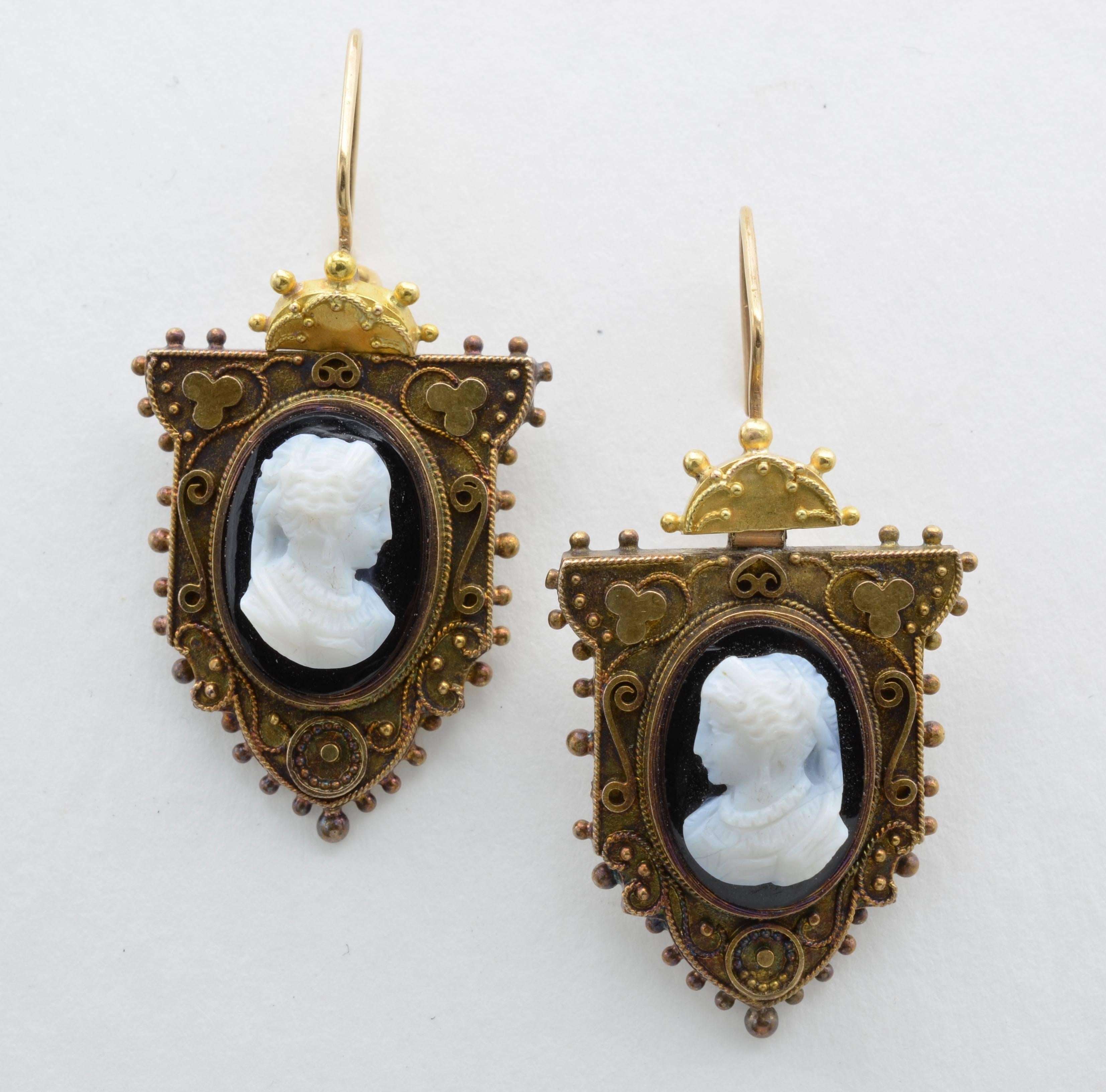 These stunning cameo and gold earrings are intricately detailed with spirals and swirls carved with the profiles of regal women. Antique and from the Victorian Era, these dangling beauties have a sun-like top that hinge to the larger portrait