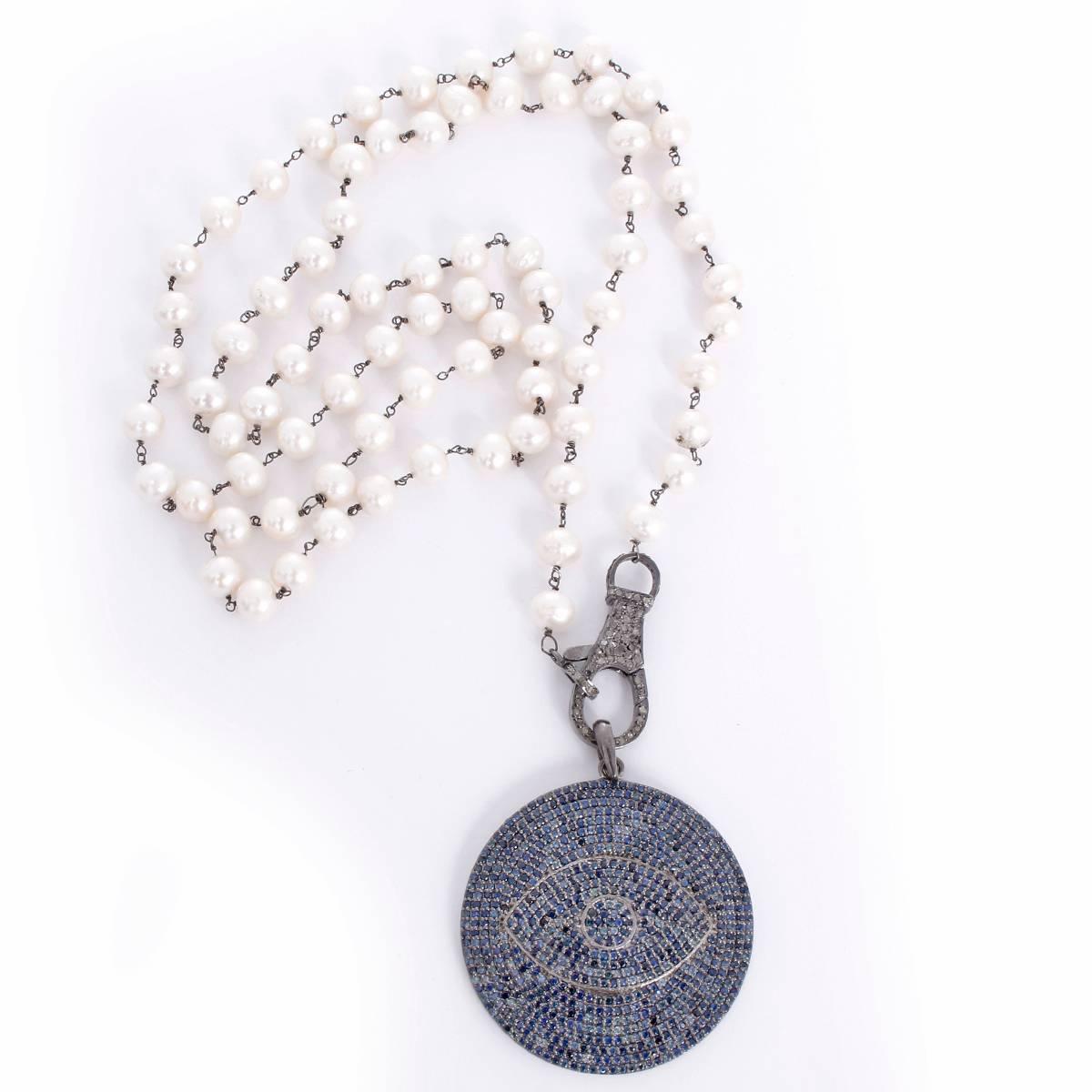 This stunning necklace features an evil eye disc pendant in blue sapphires  with a diamond clasp set in oxidized silver on a freshwater pearl chain. Pendant measures apx. 1-7/8 inches in diameter on a 36-inch chain. Total weight is 79.3 grams.