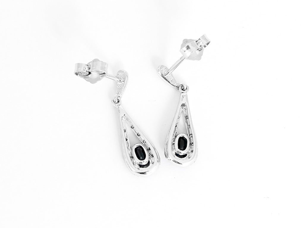 These amazing drop earrings feature oval blue sapphires and apx. 0.07 ctw. of G-color and SI-clarity round diamonds set in 14k white gold. Earrings measure apx. 3/4-inch in length. Total weight is 2.2 grams.