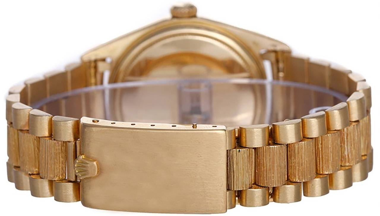 Automatic winding; non-quickset, 26 jewels; acrylic crystal. 18k yellow gold case with barked bezel (36mm diameter). White dial with stick markers. 18k yellow gold President bracelet with barked center links and buckle clasp. Pre-owned with box and