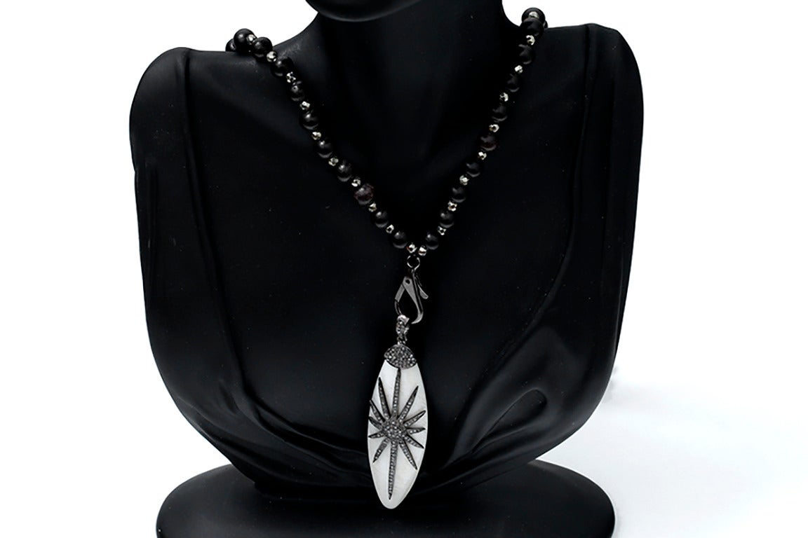 Ce collier est composé de perles en bois et d'un pendentif en os de bœuf avec un motif en étoile composé d'environ 0,39 carats de diamants pavés en argent sterling. Le collier mesure environ 36 pouces de long et le pendentif mesure environ 3-1/2
