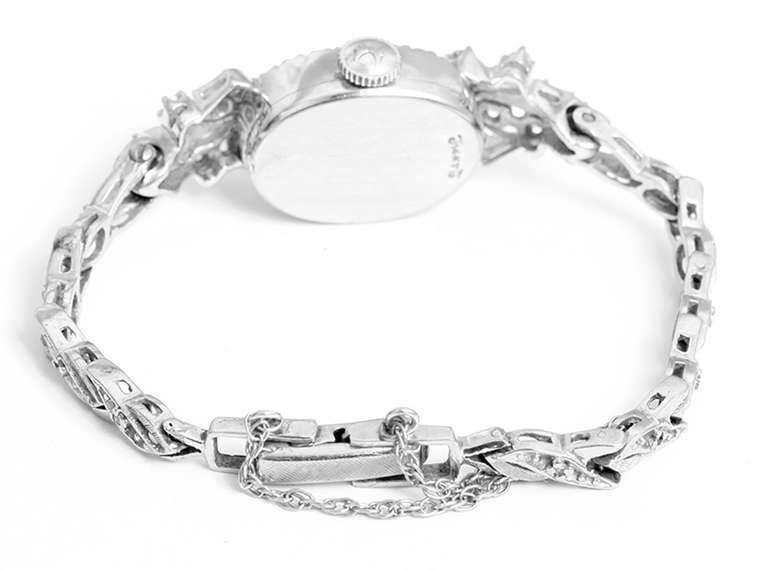 Manual-wind movement, 14k white gold case with diamond bezel and lugs, 15mm x 40mm. Silvered dial with baton markers. 14k white gold bracelet with vine-like links set with diamonds, will fit approx. 5-in. wrist.