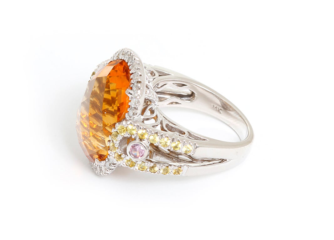 This amazing ring features one citrine bordered by diamonds with accenting yellow and pink sapphires on each side. Ring measures apx. 1-inch in width and apx. 7/16-inch in height. Total weight is 11.9 grams.