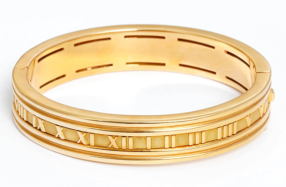 This Tiffany & Co. Atlas bracelet features rubies and Roman numeral designs in 18k yellow gold. Bracelet measures apx. 1/2-inch in width and fits up to a 7-inch wrist. Total weight is 56.0 grams. Signed 