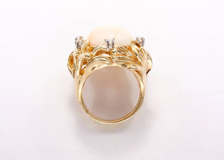 This charming yellow gold ring features an oval coral cabochon measuring apx. 18.51 mm x 14.89 mm centered by five round brilliant cut diamonds weighing approximately 0.20 carat total. It is a size 7.5 with a total weight of 16.4 grams.