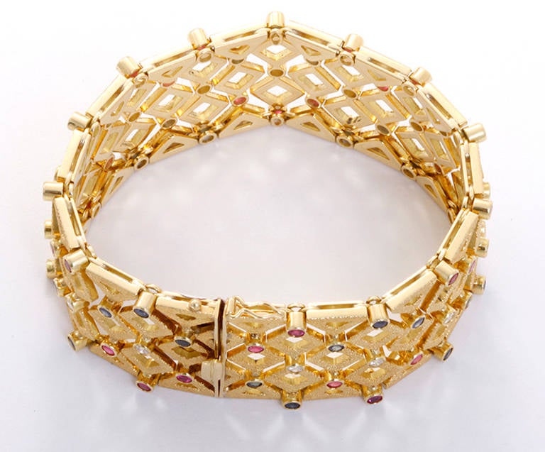 This wide lattice bracelet has a beautiful 18k yellow gold textured matte finish. It features 1.5 carats of diamonds and 7 ctw. of rubies and sapphires. It is apx. 7-3/8 inches in length and 1-1/8 inches in width with a total weight of 91.1 grams.