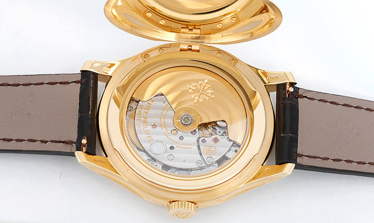 Automatic movement with date. 18k yellow gold case, hinged cover over sapphire crystal case back, 39mm diameter. Ivory-colored dial with gold dagger hour markers. Strap with 18k yellow gold Patek Philippe buckle. Unused with Patek Philippe box and