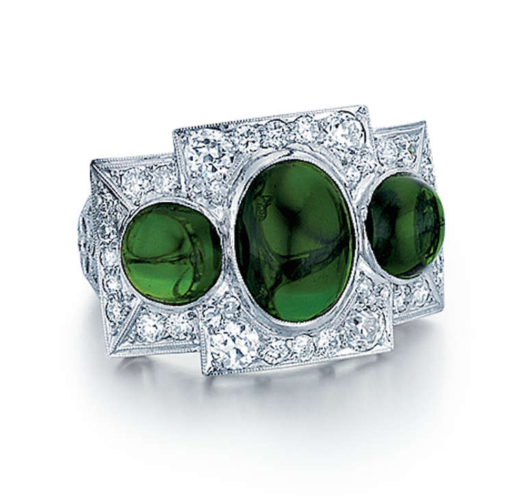 L'anello Art Deco a tre pietre è composto da platino con due pietre diopside al cromo rotonde e ovali tagliate a cabochon, accentate da diamanti rotondi.  Ci sono 36 diamanti per un totale di 1,75 carati, colore G-H e purezza VS.  L'anello è una