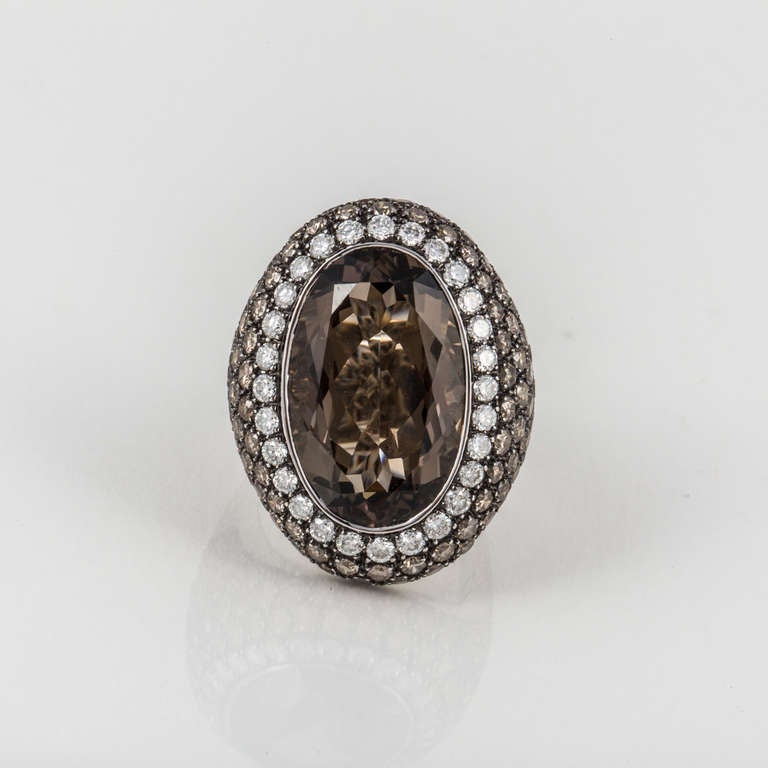 This 18kt white gold ring features a large oval smoky quartz in the center, surrounded by 122 white and brown diamonds weighing 4.90 carats total weight. The ring is currently a size 7.