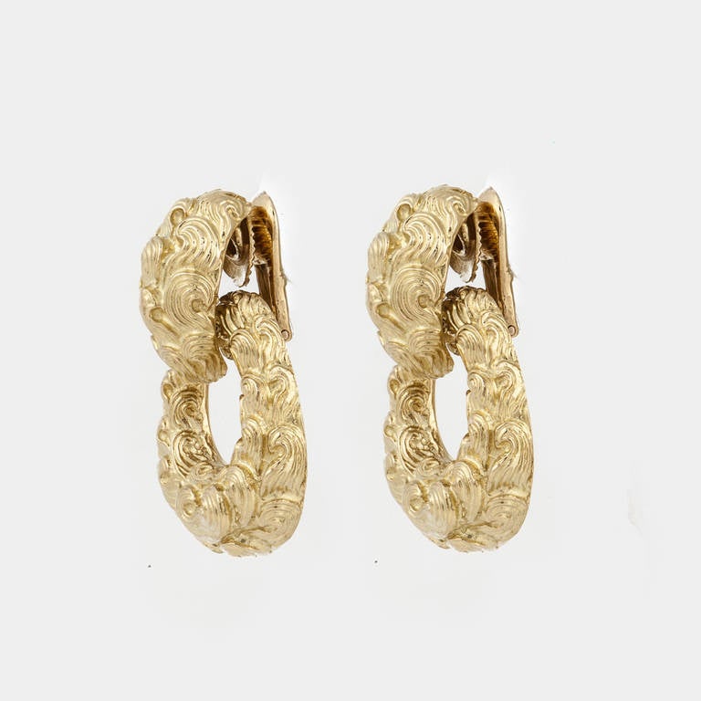 David Webb doorknocker style earrings composed of 18K yellow gold with a scroll like design on the finish.
