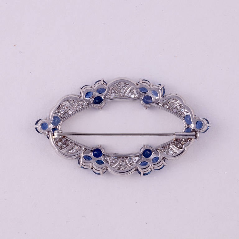 Platinum brooch featuring round diamonds and round blue sapphires. There are 74 round diamonds that total 1.40 carats, G-I color and VS-SI clarity.  There are 18 blue sapphires that total 6.65 carats.  