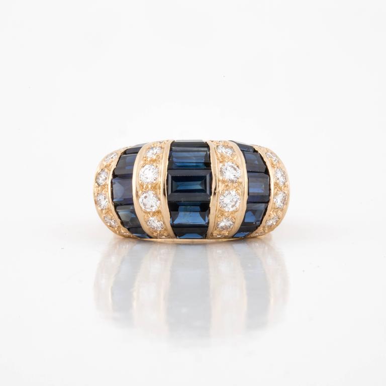 Oscar Heyman Bros. ring composed of 18K yellow gold with calibré-cut blue sapphires and round brilliant-cut diamonds.  The 24 round diamonds total 0.65 carats, G-H color and VVS-VS clarity. Presentation area measures 7/8 inch by 3/8 inch by 1/4 inch