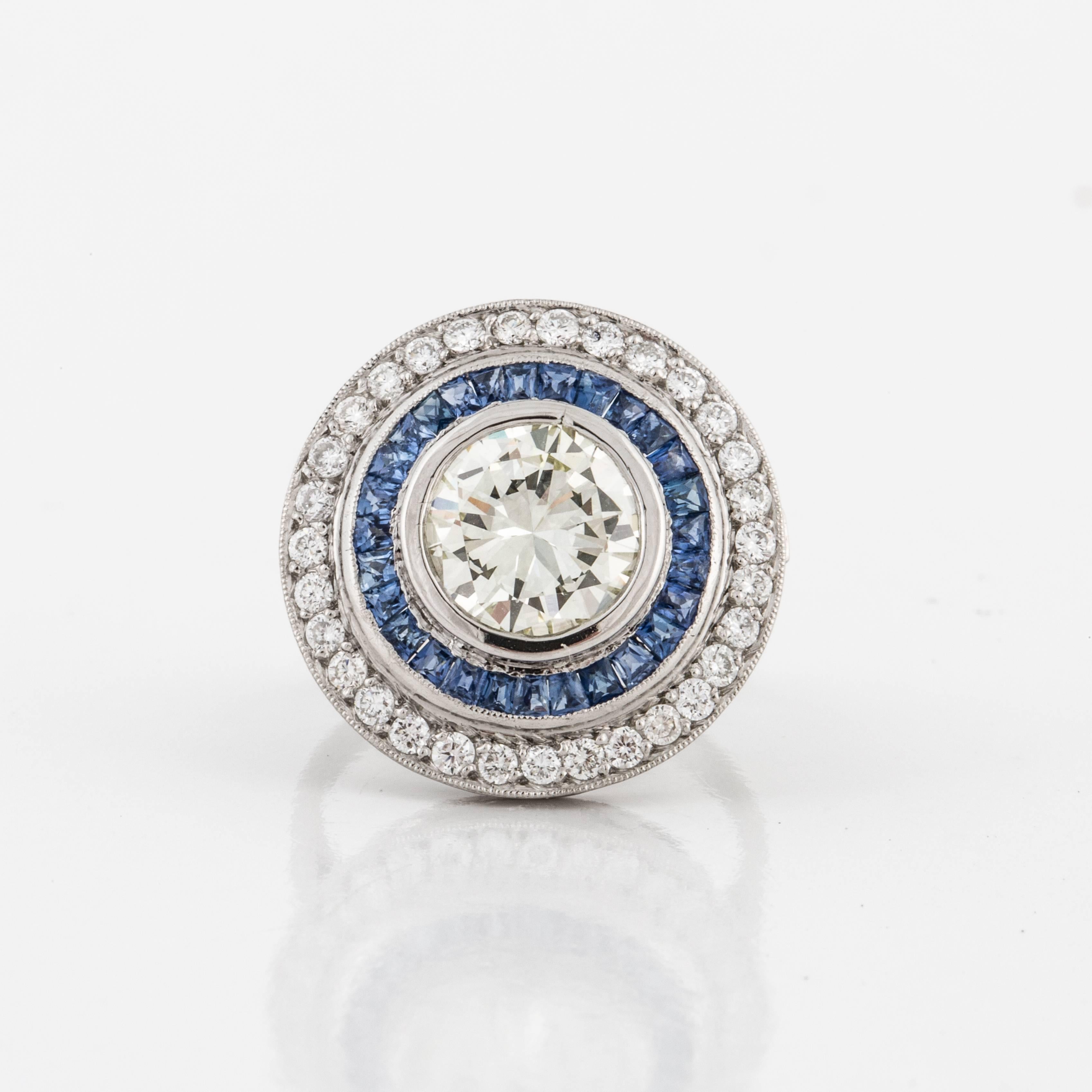 Contemporary target ring composed of platinum with diamonds and sapphires.  The center diamond is a round brilliant-cut, 2.75 carats, M color, and VVS2-VSi1 clarity.  There are 41 round diamonds totaling 0.75 carats, G-H color and VS2-VS1 clarity. 