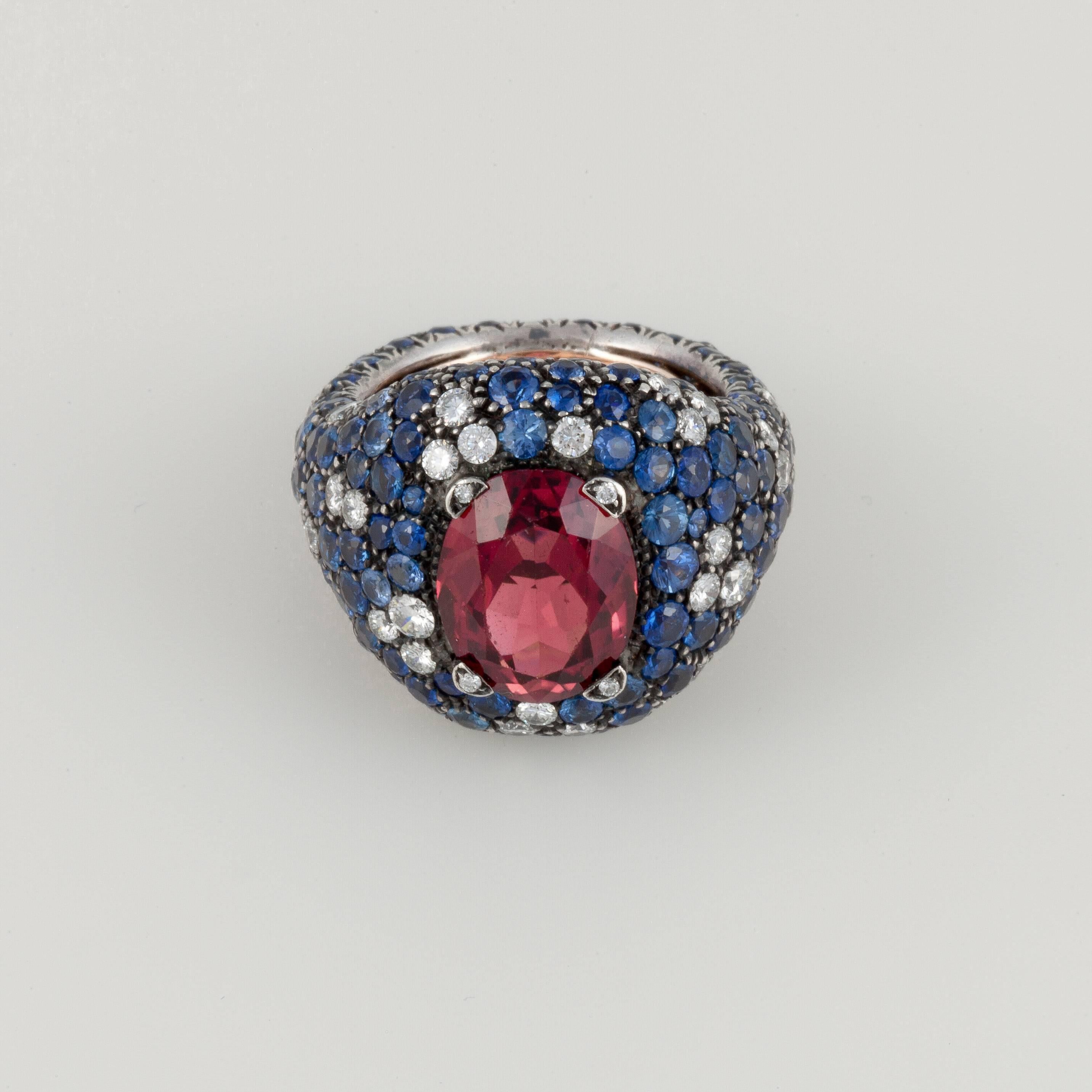 This dome style ring composed of 18K yellow gold and stainless steel features an oval rubellite stone surrounded by round blue sapphires and diamonds.  The rubellite totals 5 carats and is accented by 8 carats of sapphires and 2.50 carats of