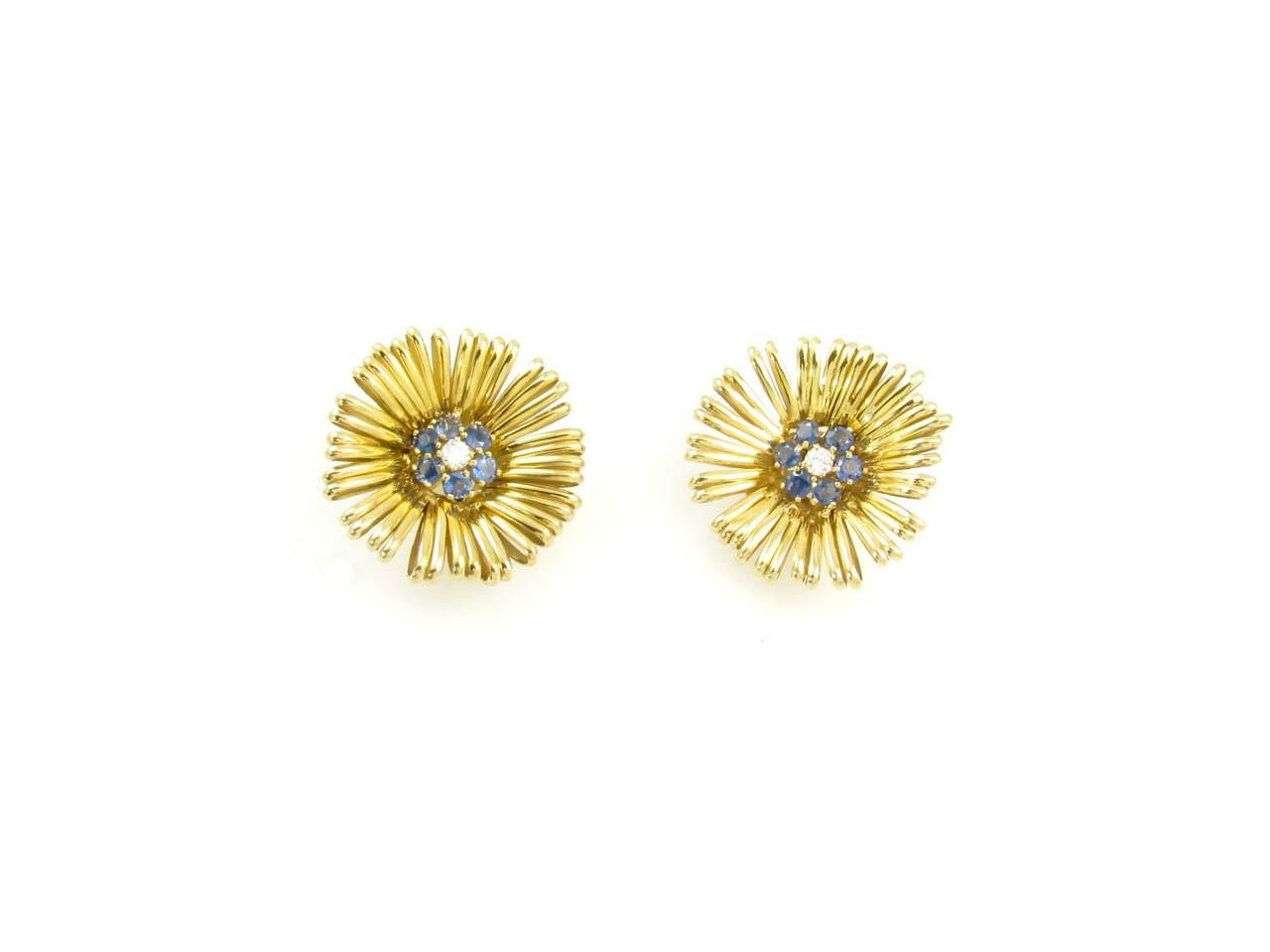 A pair of 18 karat yellow gold wire form stylized flower earrings set with a sapphire and diamond cluster center, circa 1955.  The 18 karat earrings are set with 14 karat yellow gold heavy clip mechanisms.  The centers are each set with 6 round