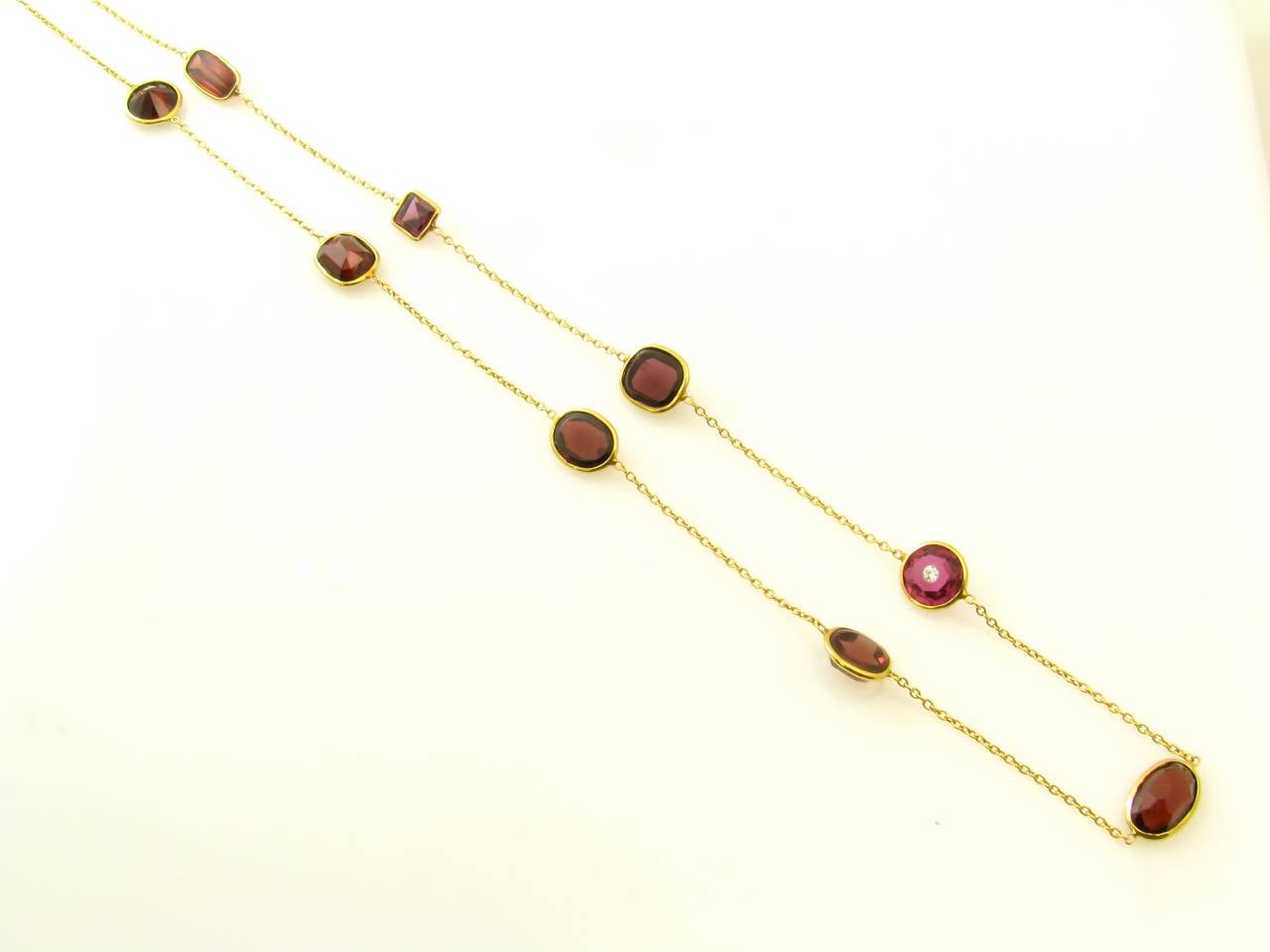 An 18 karat yellow gold, collet set garnet and pink tourmaline necklace with a toggle closure, Signed Renee Lewis 18 KT.  The cable link necklace is set with 10 faceted garnets and a pink tourmaline inset with an approximately .05 carat round