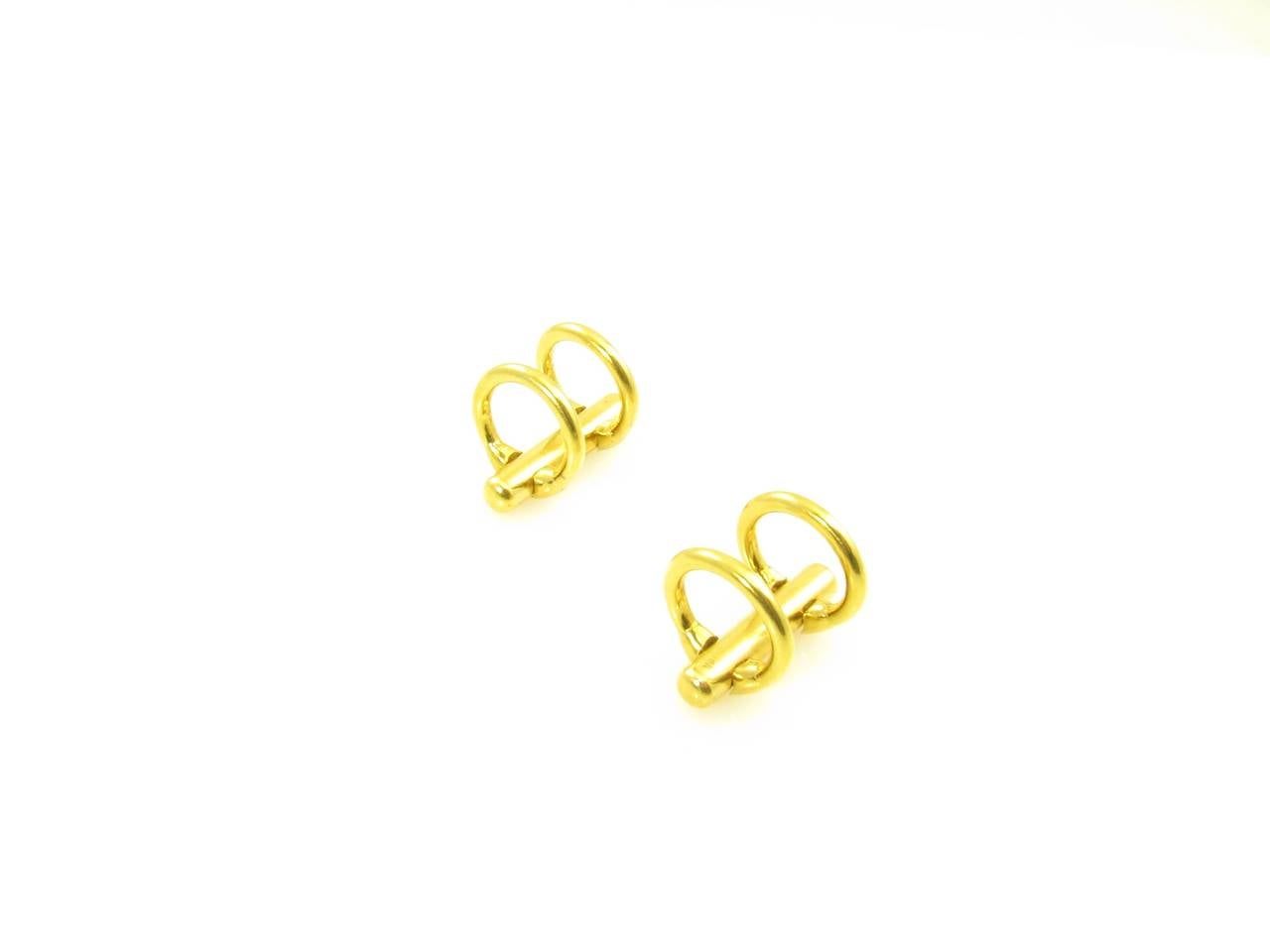 A pair of 18 karat yellow gold double ring style cufflinks.  Each is designed with a center tubular bar, each end with a hinged ring fastener.  The cufflinks have a gross weight of approximately 15.1 grams.