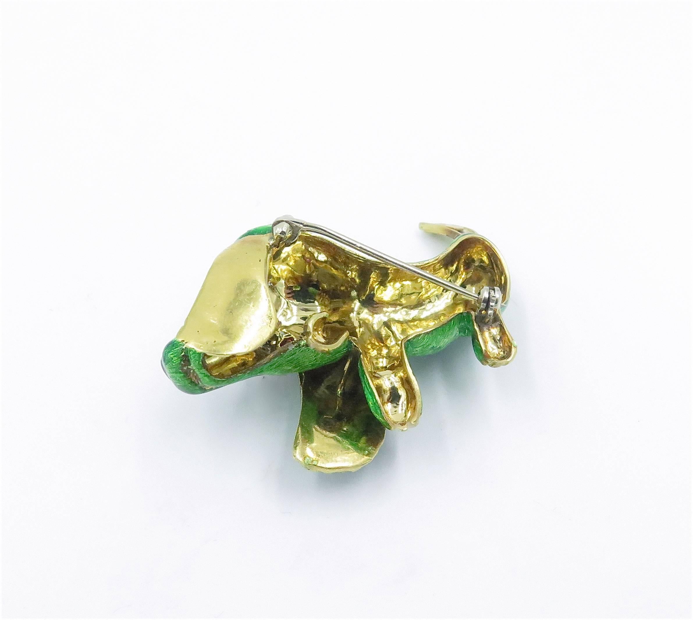 An 18 karat yellow gold, enamel, ruby and diamond dog brooch. Circa 1960. Designed as a stylized green enamel dachshund, enhanced by a marquise-cut ruby eye, with circular-cut diamond detail. Length is approximately 2 1/4 inches.  Gross weight