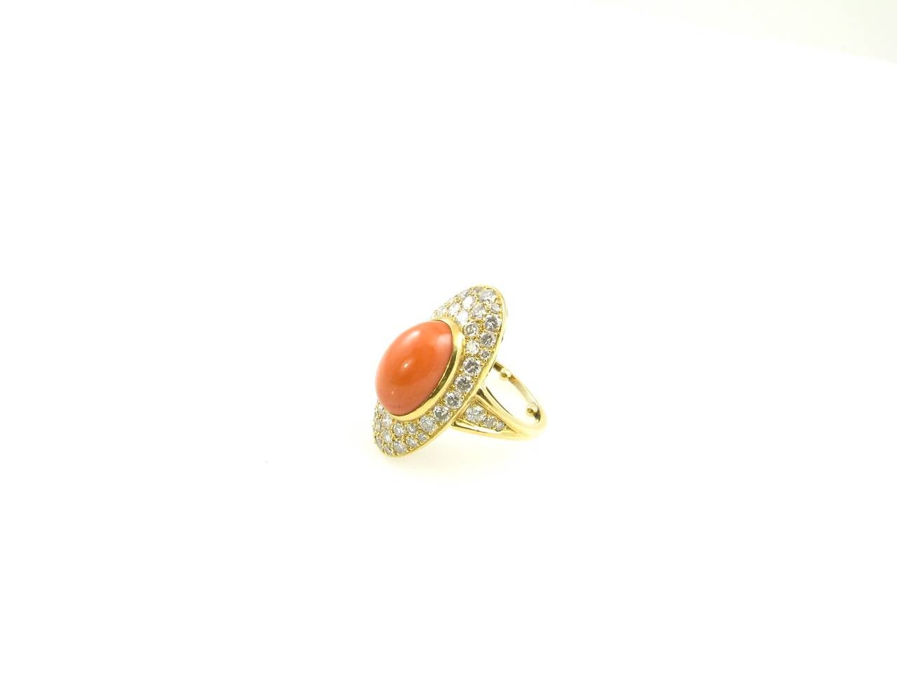 A French 18 karat yellow gold, diamond and salmon coral ring, Circa 1970.  Signed France 4971 and hallmarked with French maker’s mark and faint gold mark.  The bezel set oval cabochon coral is surrounded by an oval frame of pave set round brilliant