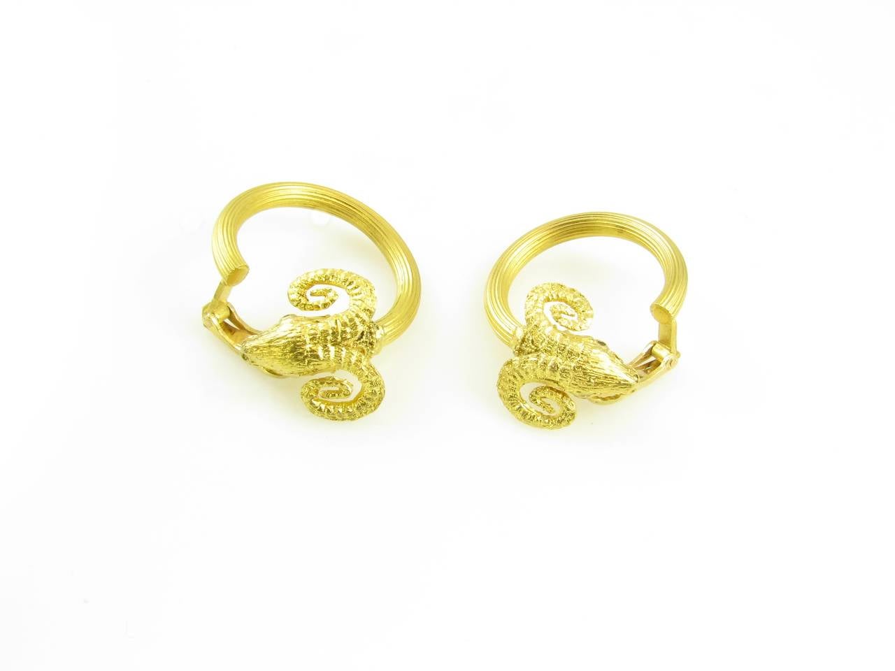 A pair of 18 karat yellow gold and ruby rams head hoop style earrings, Ilias Lalaounis, Greece, Circa 1970s.  The earrings are each designed as a ram’s head with round faceted ruby eyes, with fluted hoop style body.  The earrings have a gross weight