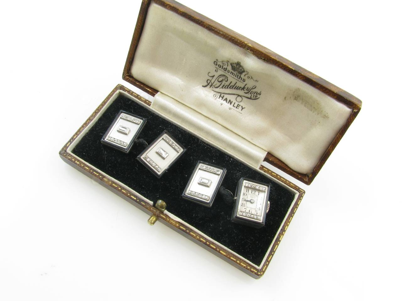 A pair of platinum, white gold, diamond-set and enamel cufflinks set with a watch, Signed Lusina, Circa 1925.  The watch is set with a nickel-finished lever movement, 16 jewels, bimetallic compensation balance, silvered matte dial Arabic numerals,