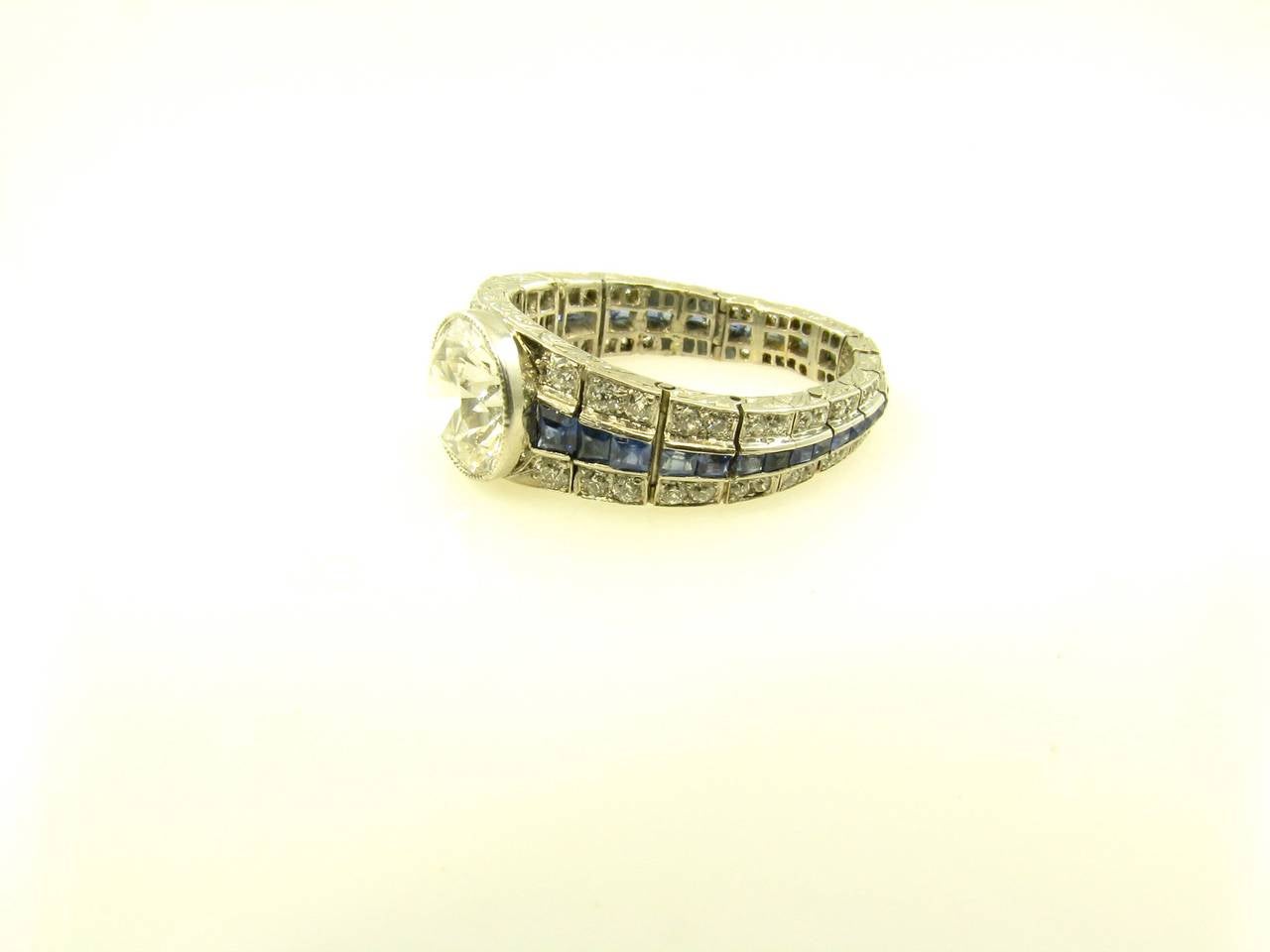 An Art Deco, platinum, diamond and sapphire ring, Tiffany and Company, Circa 1925.  Designed as a flexible band that is channel set with graduated square cut sapphires flanked by a row of pave set transitional cut round diamonds on each side.  The