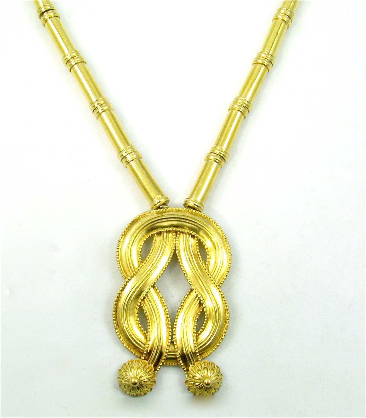 A 22 karat yellow gold “Hercules Knot” necklace, Ilias Lalaounis, Greece, Circa 1970s.  The long gold necklace  with tubular clasp is designed with tubular gold links on a braided chain, suspending a Hercules knot with gold floral bosses.  The