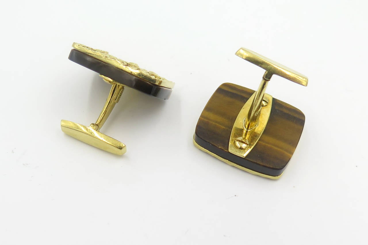 A pair of 18 karat yellow gold and tigers eye cufflinks, Cartier, Circa 1970s.  Signed Cartier 18K 28511.  The oblong tigers eye cufflinks are mounted with a textured gold openwork plaque and gold swivel back fittings.  The cufflinks have a gross