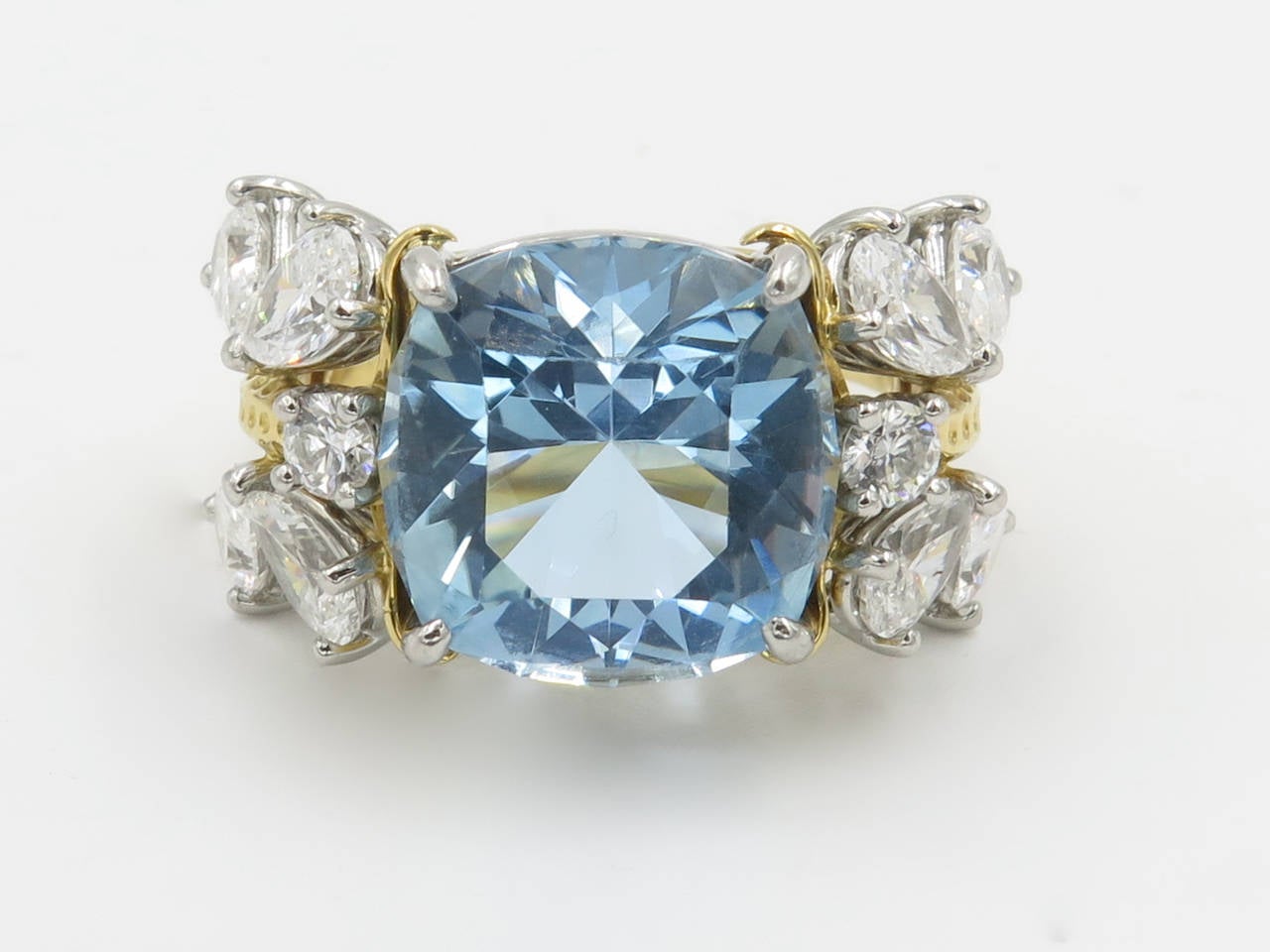 An 18 karat yellow gold, aquamarine and diamond ring. Signed Tiffany & Co. Schlumberger. The ring centers a cushion cut aquamarine flanked by (8) pear shaped diamonds and (2) round brilliant cut diamonds. The ring is set with a total of 2.53 carats