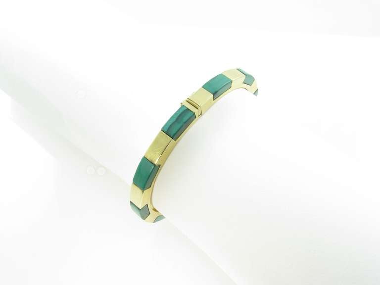 An 18 karat yellow gold and malachite hinged bangle bracelet.  Circa 1970s.  The bracelet contains 10 rectangular inset malachite sections.  The bracelet has a gross weight of approximately 30.3 grams and has an inner circumference of 7 1/4 inches.