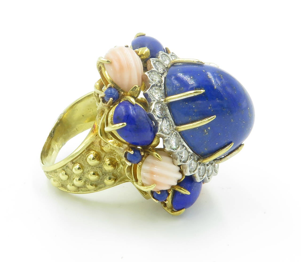 An 18 karat yellow gold, lapis lazuli, carved coral and diamond ring, Circa 1960s.  The oval cluster style ring is set with a cabochon lapis lazuli in the center, surrounded by a white gold cluster of 20 round brilliant cut diamonds weighing a total