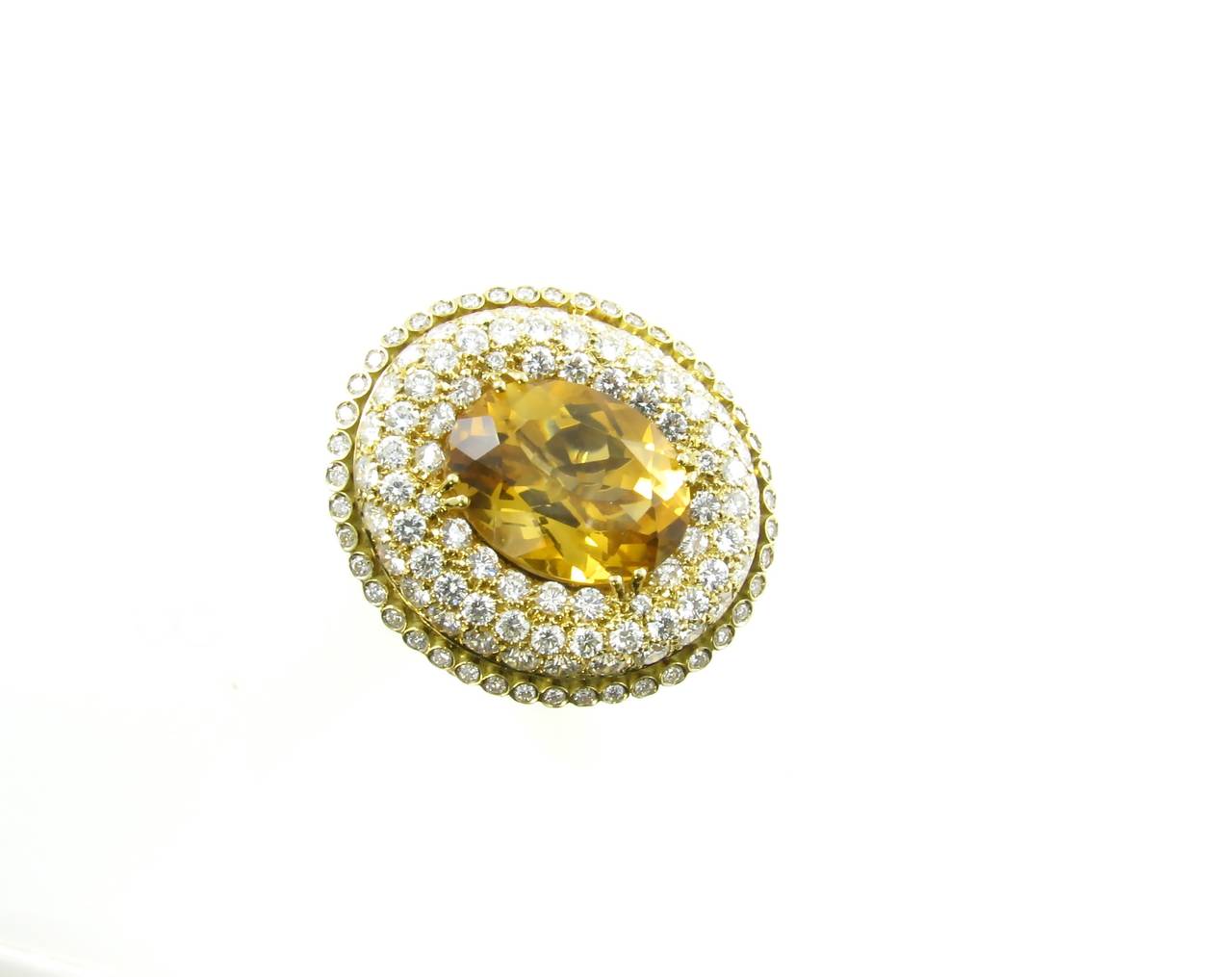 An 18 karat yellow gold, diamond, yellow sapphire and citrine ring, by Valente Milano, Italy, circa 1990s.  The ring is designed with a center oval faceted citrine set within a pave diamond surround with a collet set diamond border.  The 121 round