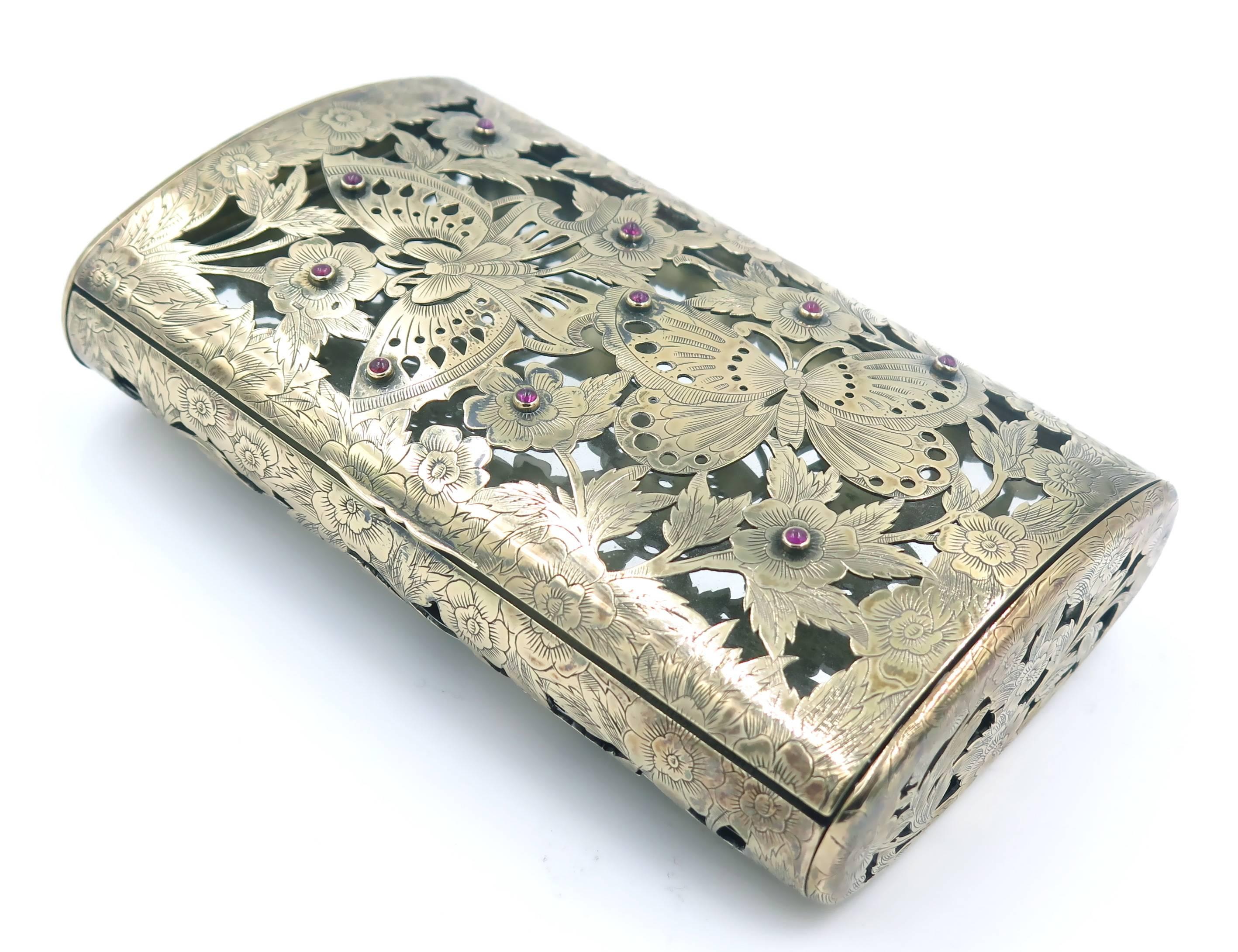 A silver, 18k rose gold topped and ruby vanity case, Boucheron, French. Circa 1940. The bombe rectangular case in a gold pierced pattern of flowers and butterflies, opening to reveal a powdered compartment and two lipstick cases. numbered 61. 803,