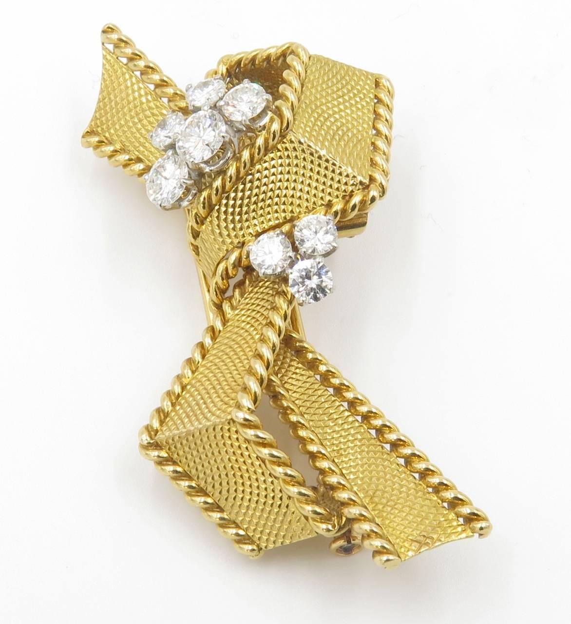 An 18 karat yellow gold and diamond brooch, Mauboussin, Paris. Circa 1950. Designed as a textured gold ribbon, enhanced by round brilliant-cut diamonds. eight (8) diamonds weigh approximately 2.00 carats, G/H color, VS-SI clarity. Signed Mauboussin,