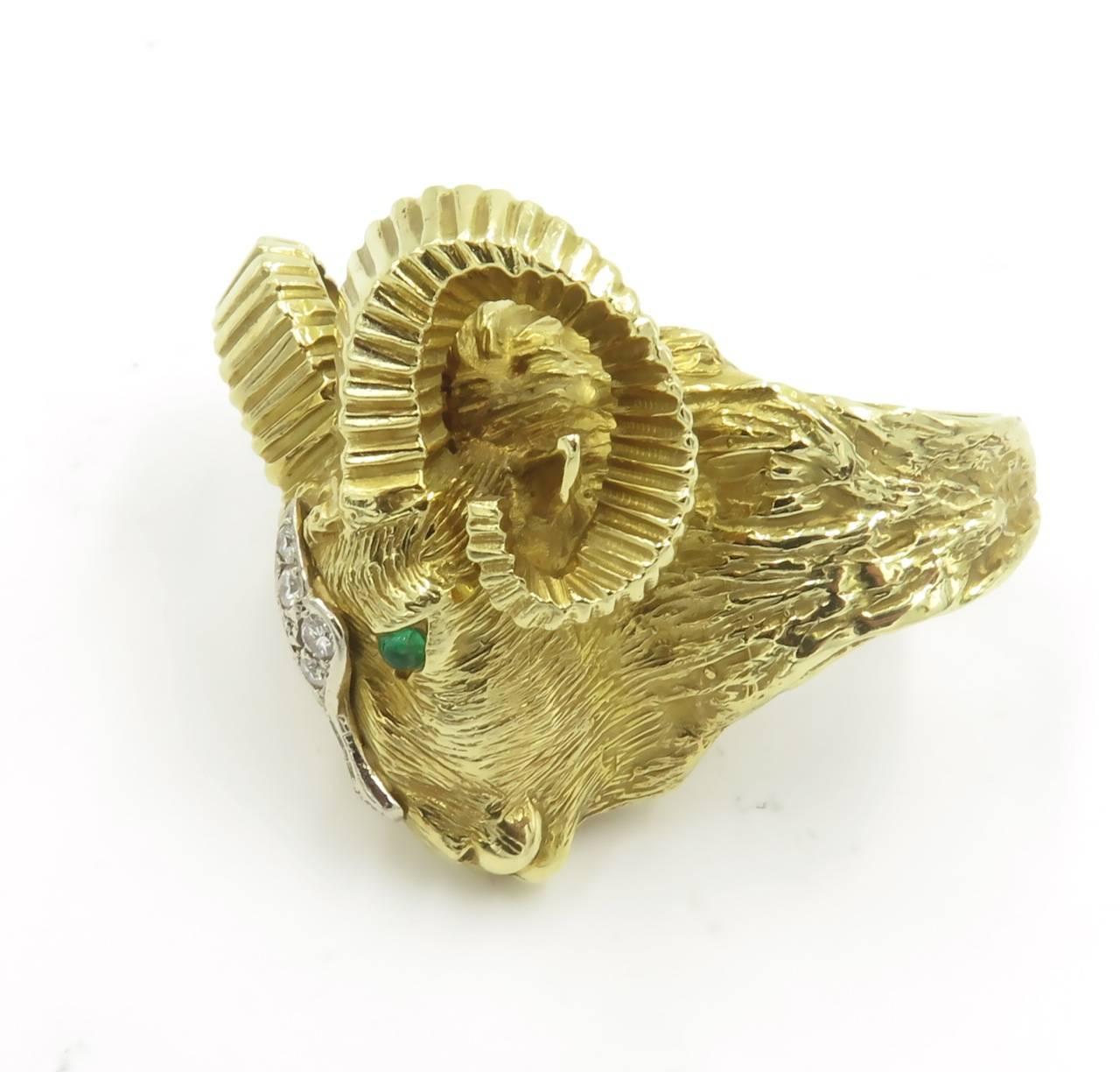 A 14 karat yellow gold, diamond and emerald ram’s head ring, La Triomphe. Circa 1960. The textured gold ring with fluted gold horns, enhanced by cabochon emerald eyes and circular-cut diamond detail. Six (6) circular-cut diamonds, weigh