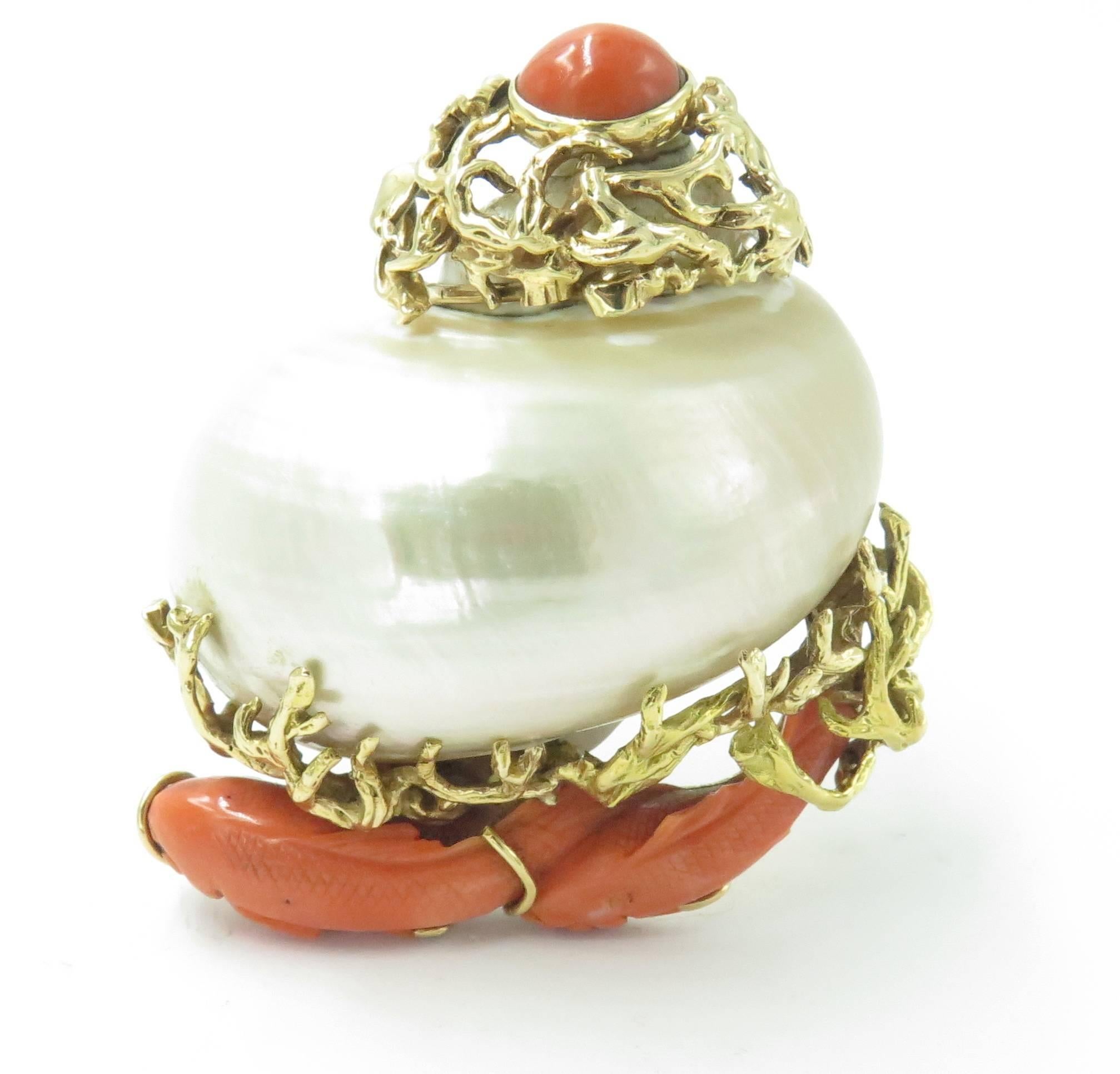 A 14 karat yellow gold, shell and coral brooch, Seaman Schepps. Circa 1960. Set with a large white turbo shell, enhanced by carved coral koi fish and textured gold seaweed, the top set with an oval coral cabochon, measuring approximately 10.00mm.