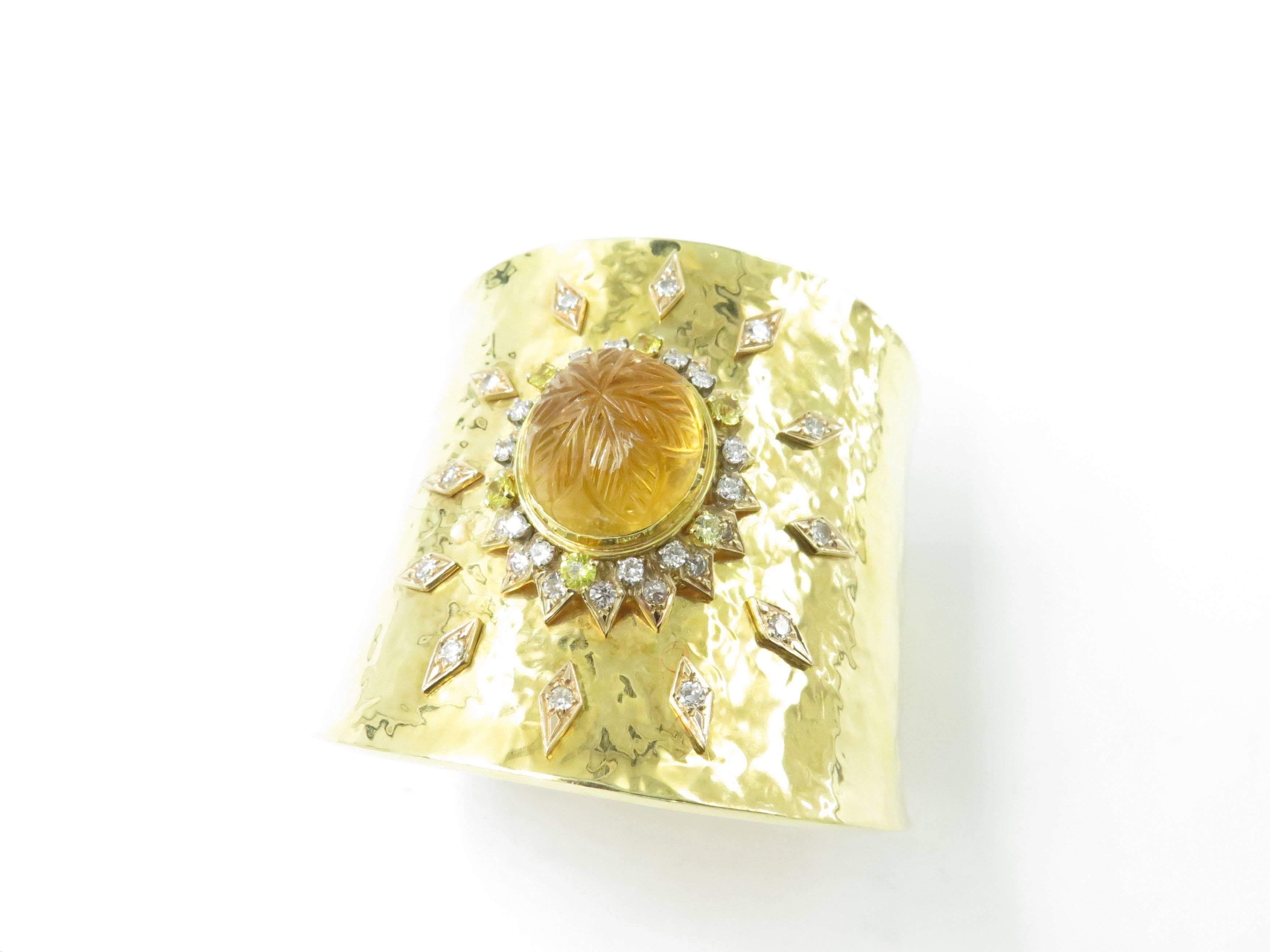 An 18 karat yellow gold, citrine, diamond and yellow sapphire cuff bracelet, Circa 1970. The hammered gold decorated with a sun burst motif, centering an oval carved cabochon citrine, measuring approximately 18.00 x 15.50. within a circular diamond