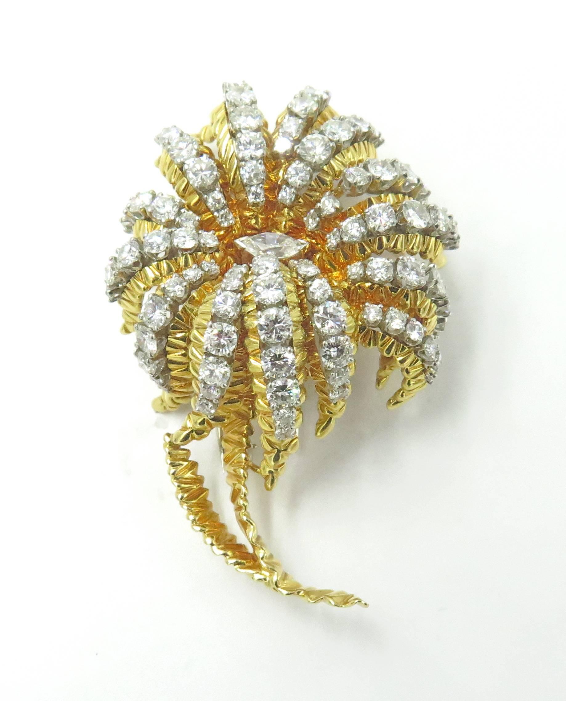 An 18 karat gold and diamond flower brooch, French. Circa 1960. Of textured gold design, the petals set with round brilliant-cut diamonds, centering a marquise-cut diamond. Ninety six (96) round and one (1) marquise-cut diamond, weigh approximately