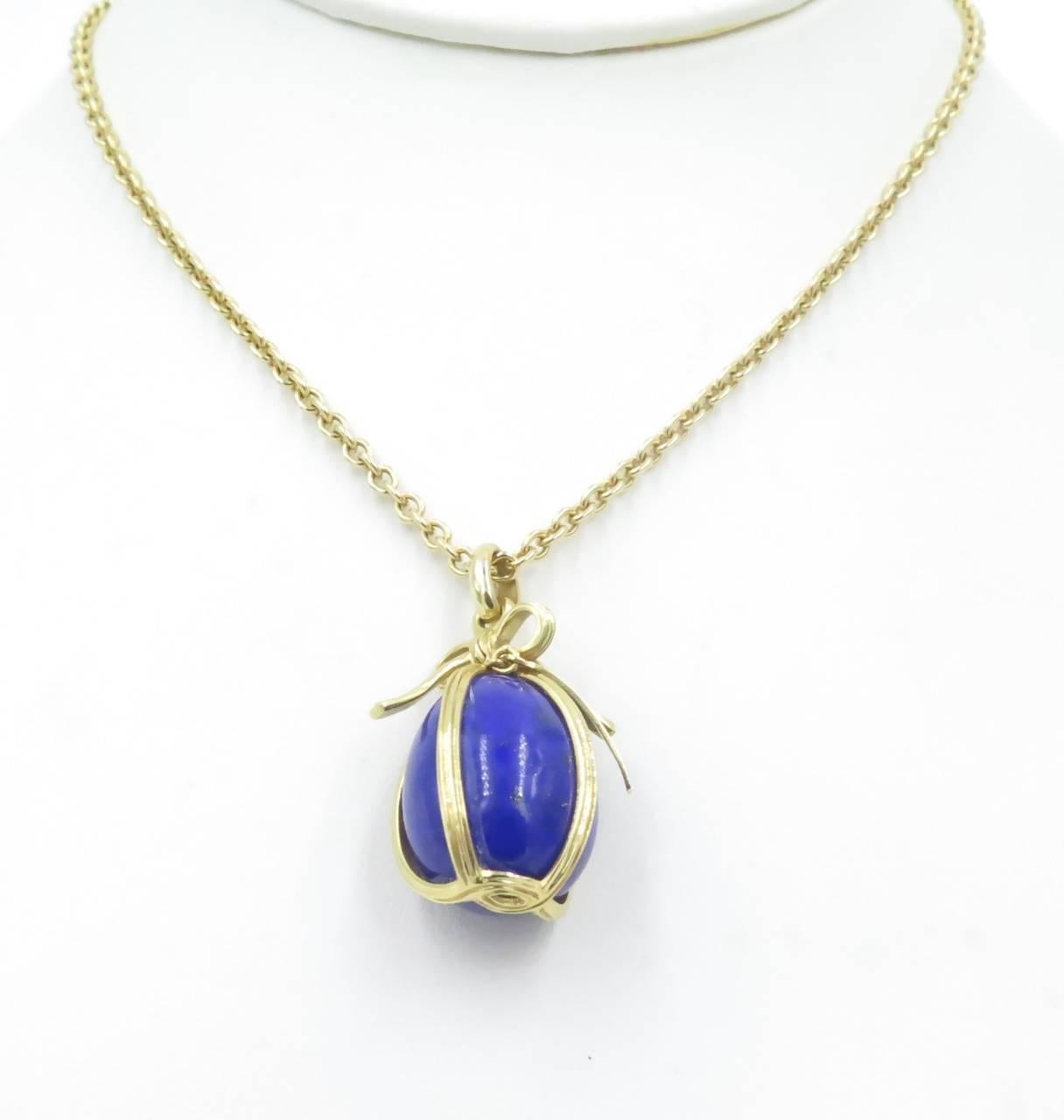 An 18 karat yellow gold lapis lazuli egg pendant necklace.  Tiffany & Co., Schlumberger.  The model is known as the large egg pendant.  Designed as a lapis lazuli egg, wrapped in a gold ribbon, suspended from an oval link chain.  Chain length is