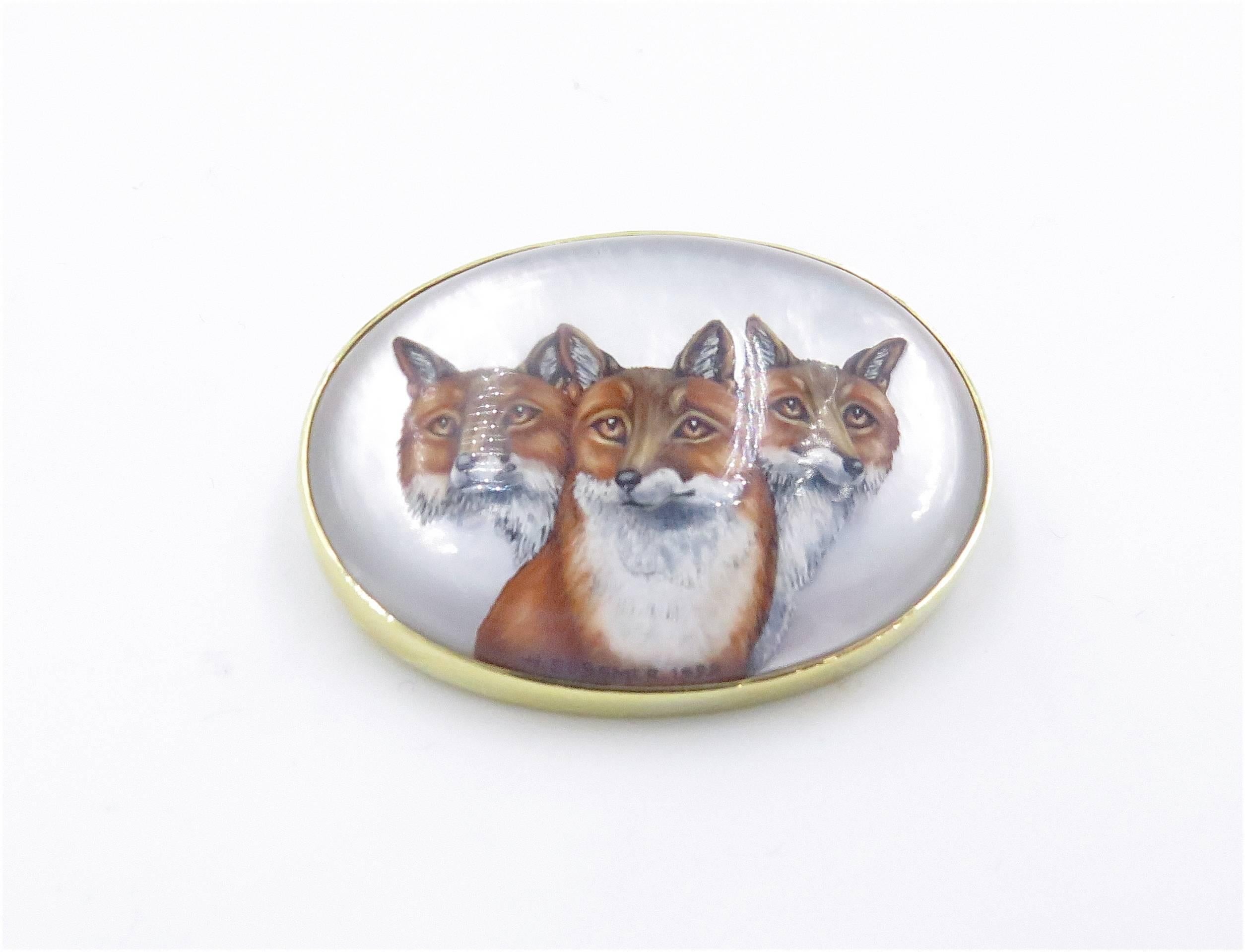 An 18 karat yellow gold, reverse crystal and mother of pearl brooch. Signed H. Bussmer, German. The oval plaque depicting (3) three foxes.  Measurements are approximately 1 1/2 x 1 1/4 inches. Signed H. Bussmer, 1999. Gross weight approximately 30.1